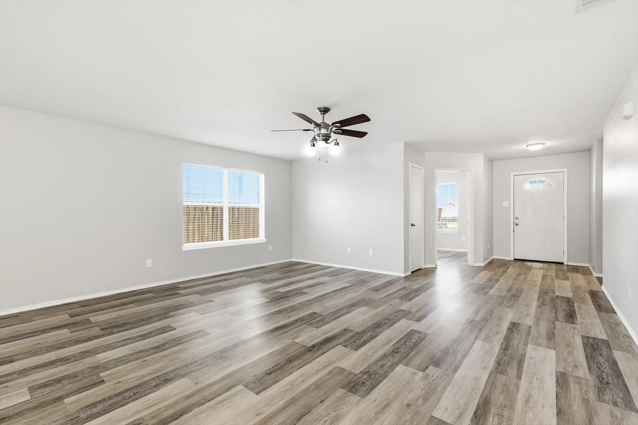Expansive room featuring wood-finish flooring, a ceiling fan with integrated lighting, and multiple windows