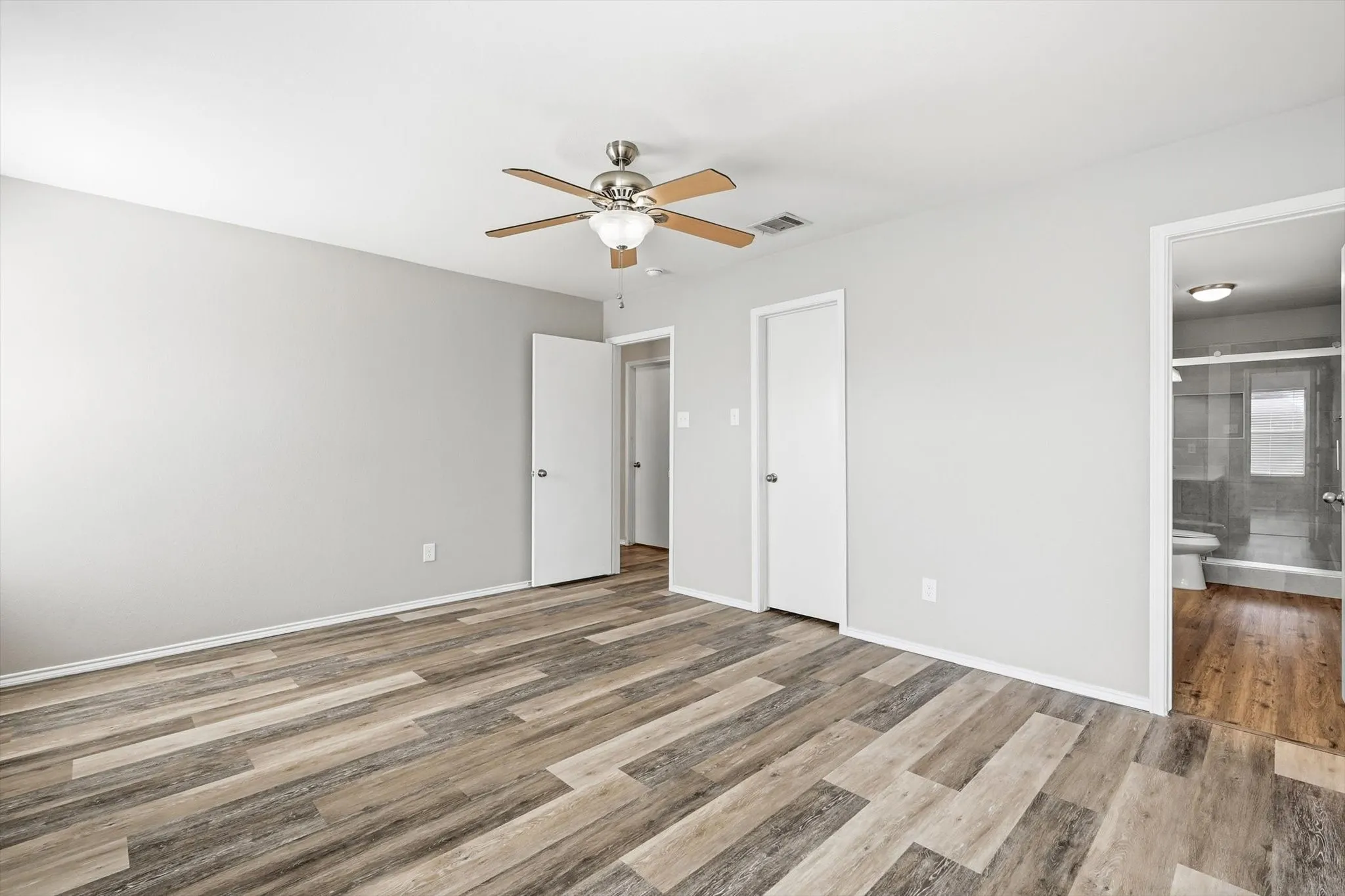Spacious room with wood-finish flooring, light gray walls, and a ceiling fan with integrated lighting