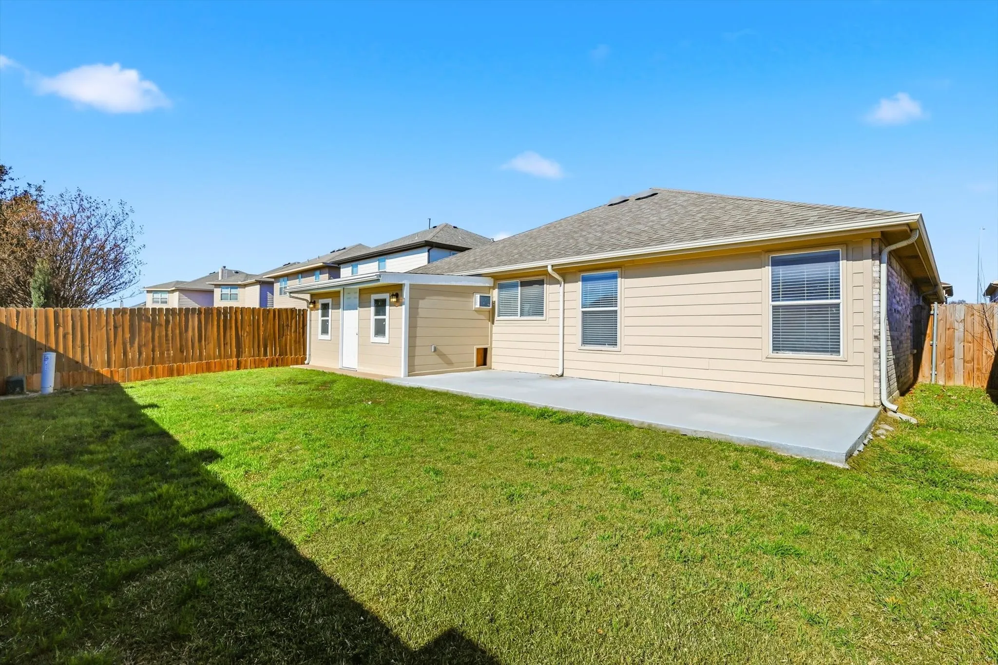 Expansive grassy area with a concrete patio, wood privacy fence, and beige siding