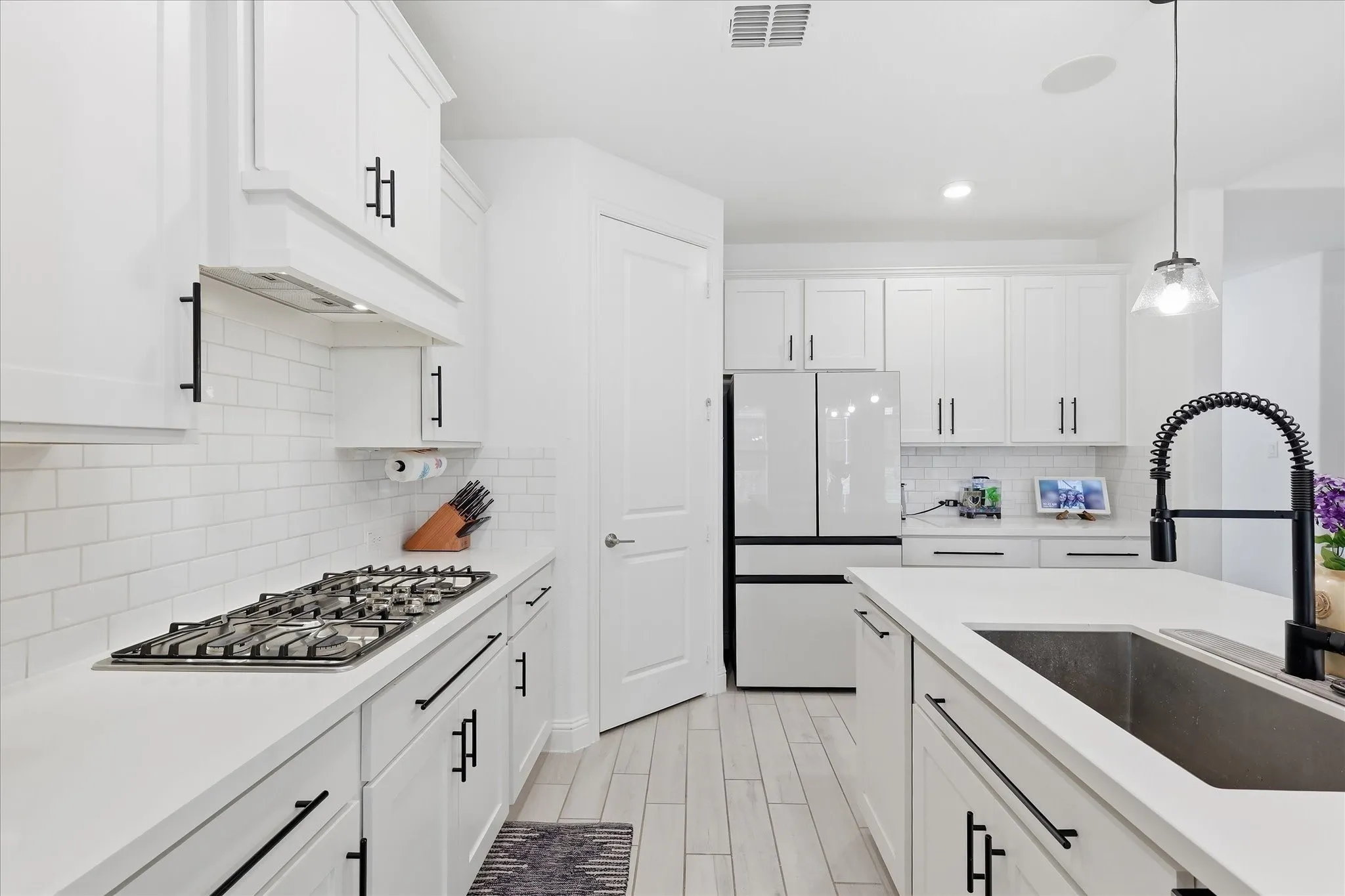 White shaker cabinetry with black hardware, subway tile backsplash, white countertops, built-in gas range, and wood-finish flooring