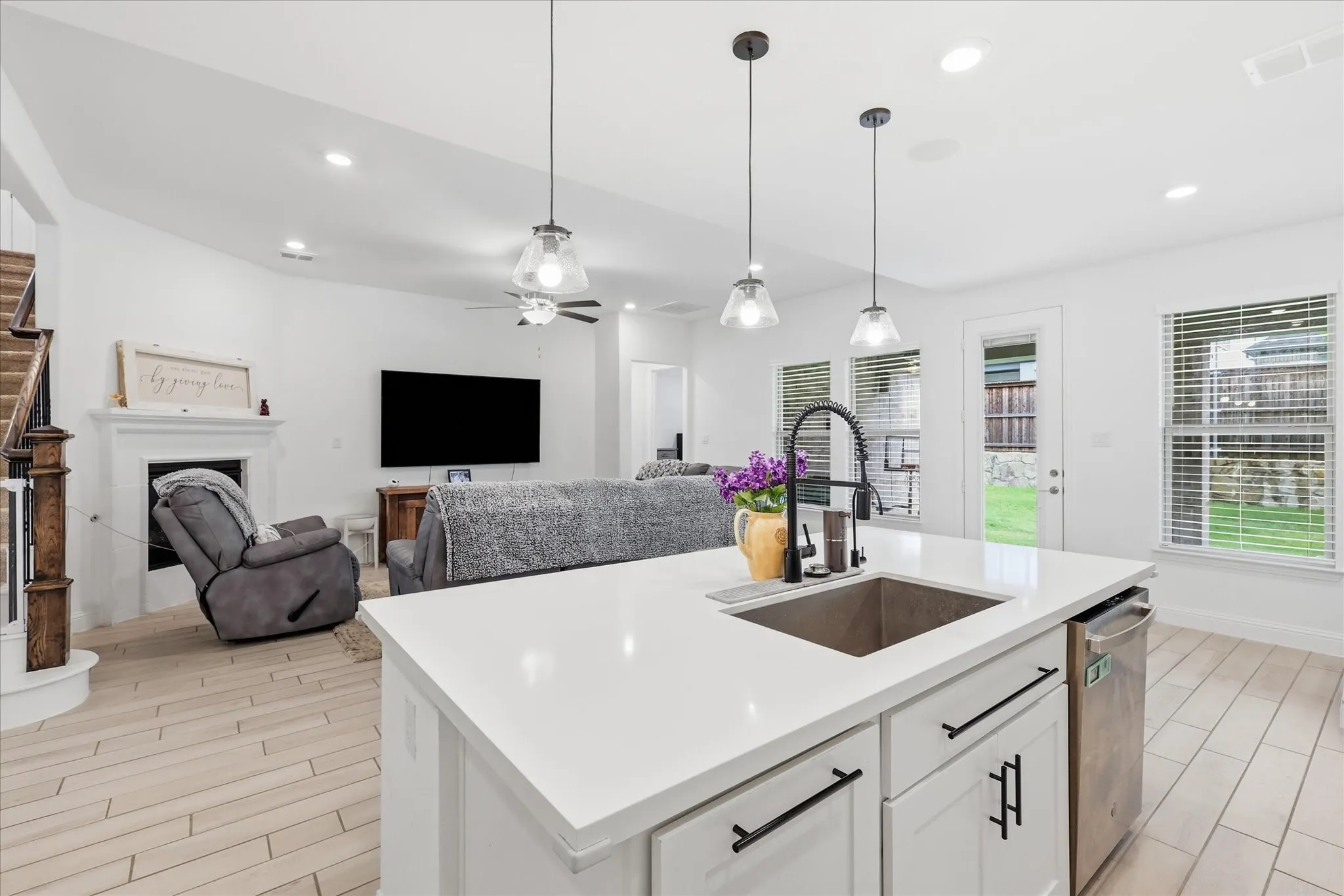 Kitchen island with a stainless steel sink and matte black faucet, open to a living area with a fireplace