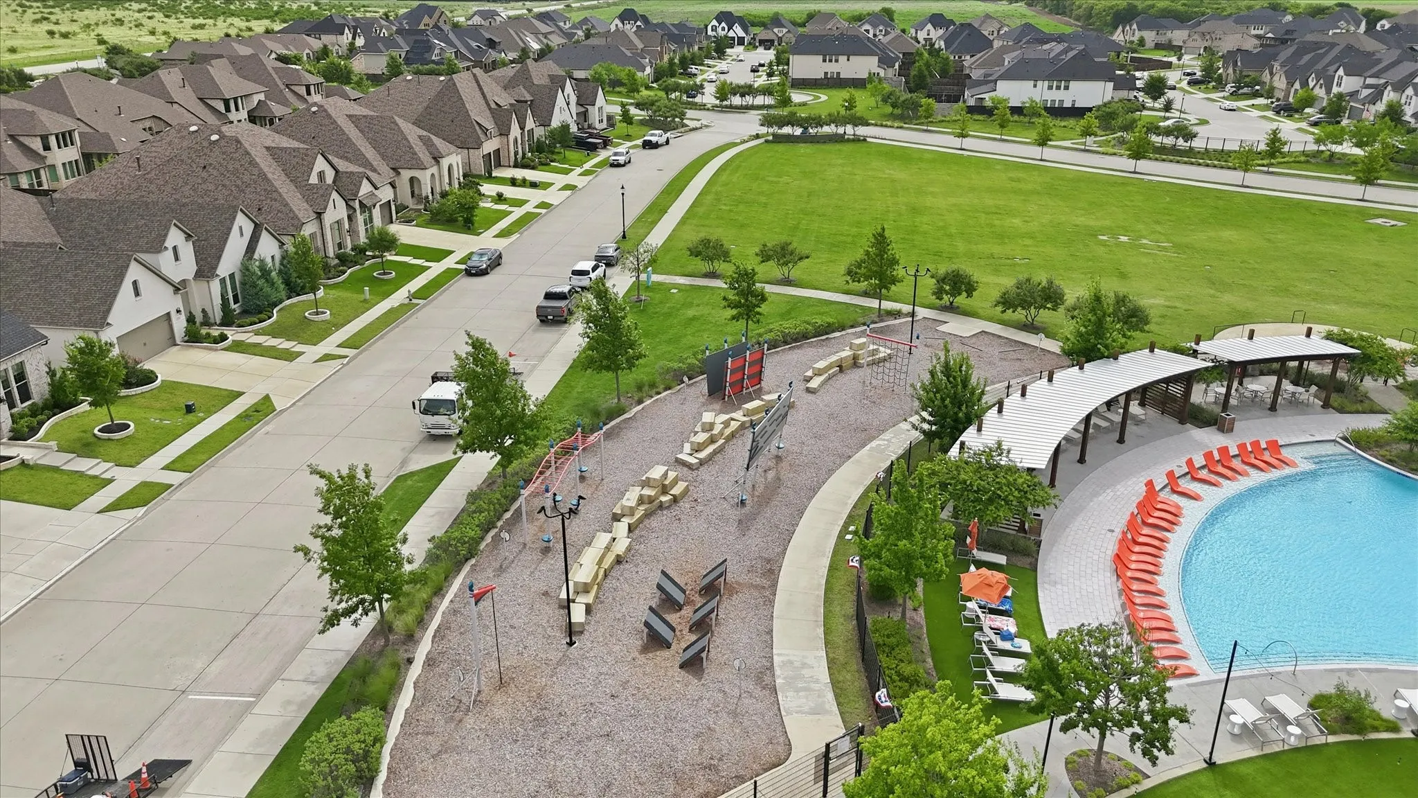 Community pool with shaded seating, adjacent children's play area, and extensive green spaces