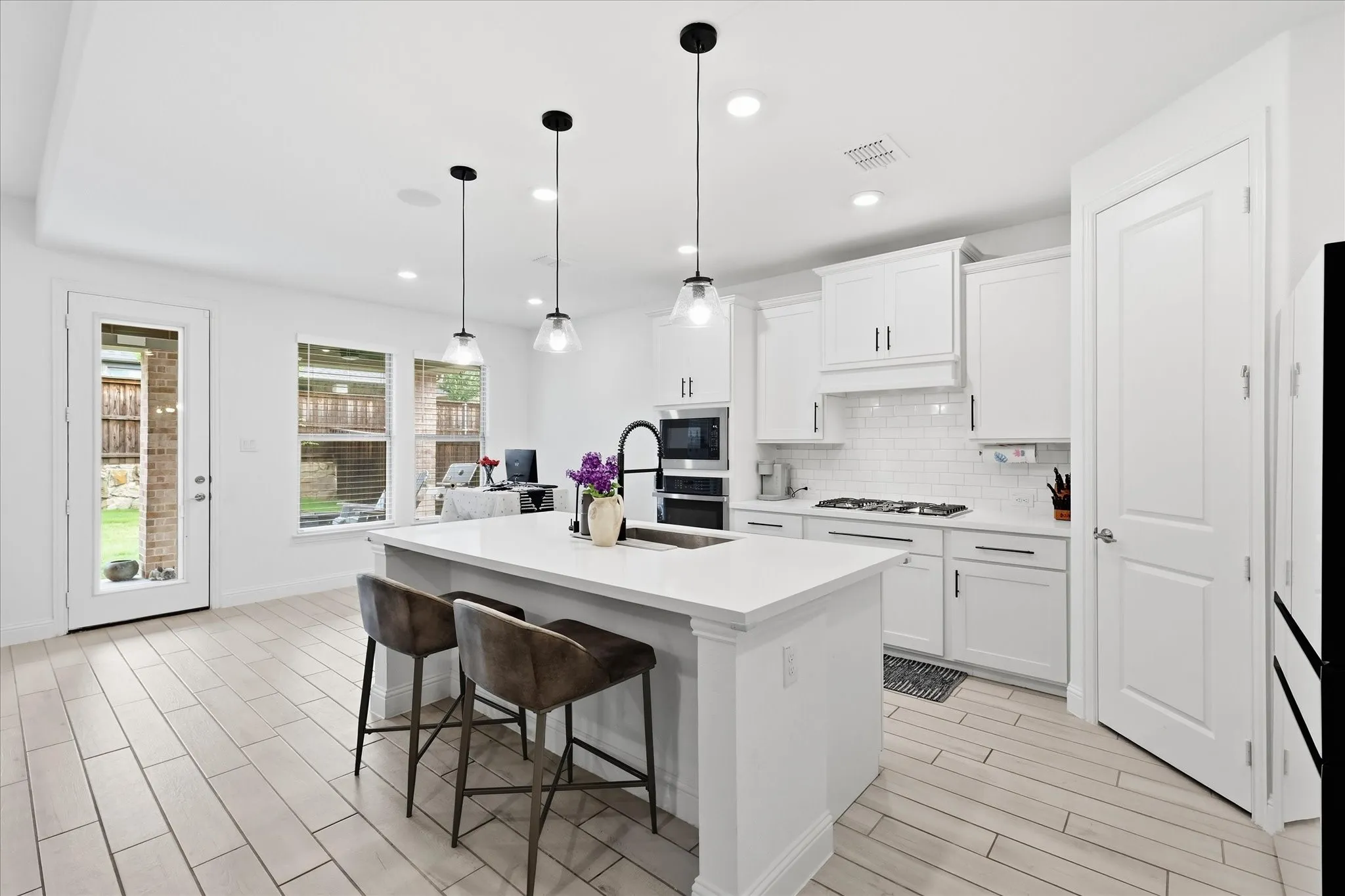 White cabinetry with black hardware, white subway tile backsplash, white quartz countertops, stainless steel appliances, and pendant lighting