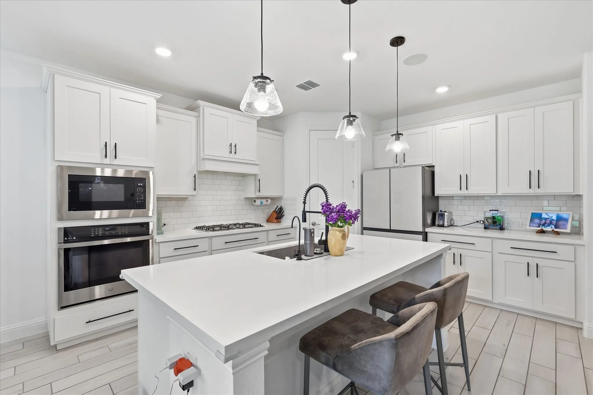 Kitchen featuring white shaker cabinetry, stainless steel appliances, a center island with pendant lighting, a subway tile backsplash, and light-toned wood-finish flooring