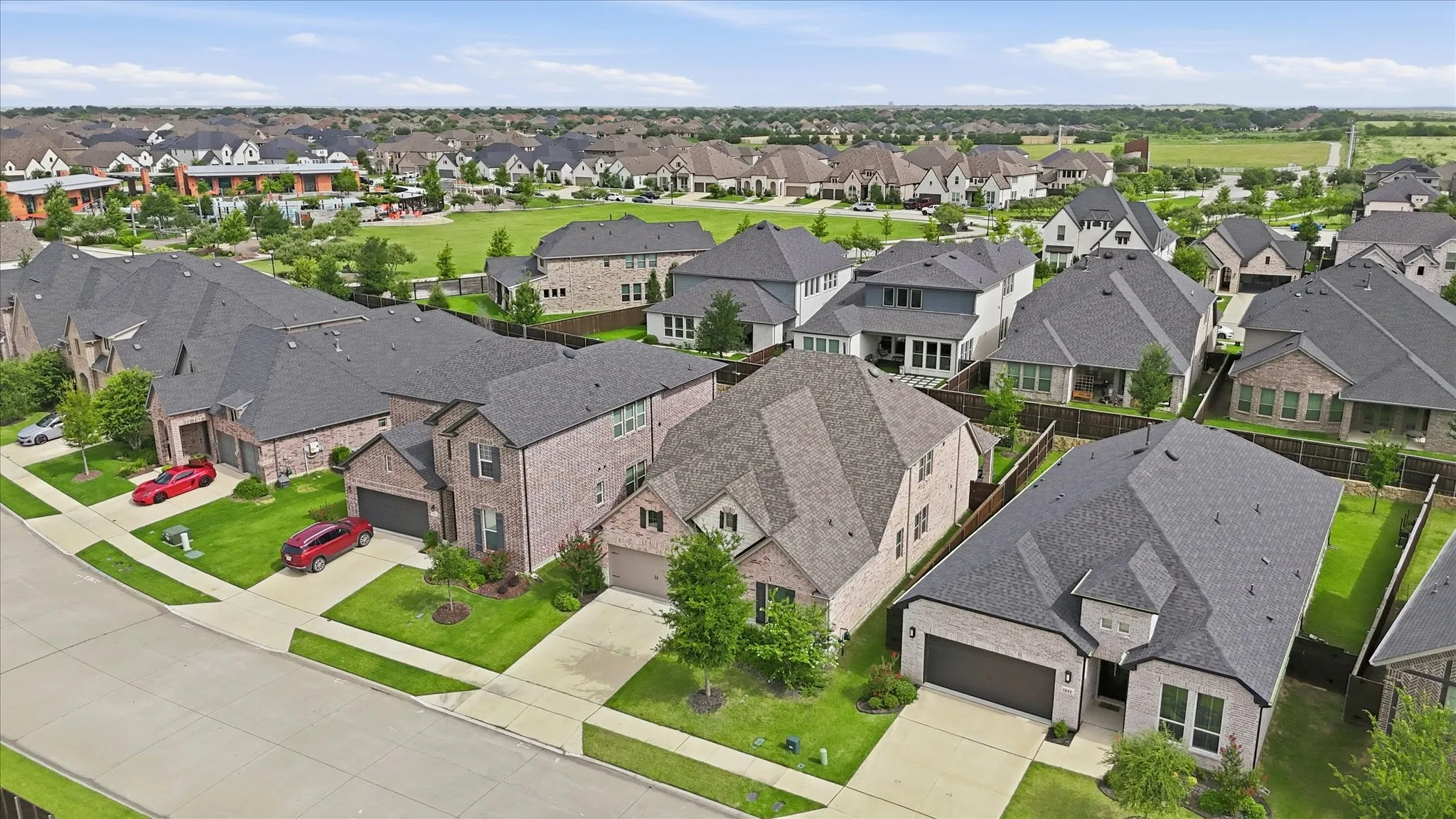 Expansive neighborhood featuring multiple single-family homes with brick and stone exteriors, manicured lawns, and attached garages