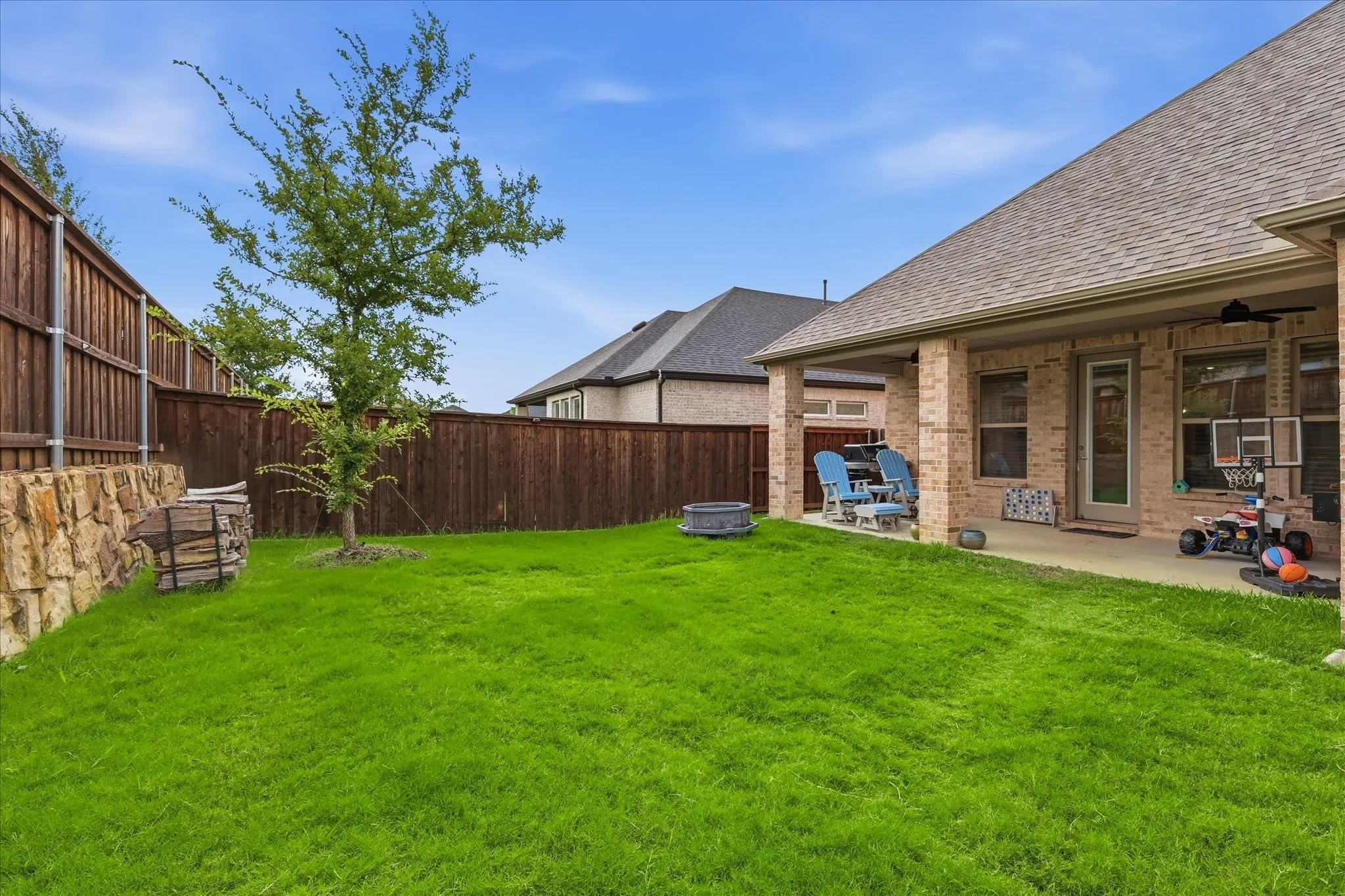 Expansive grassy lawn with a covered patio featuring a ceiling fan, brick pillars, and a wood privacy fence