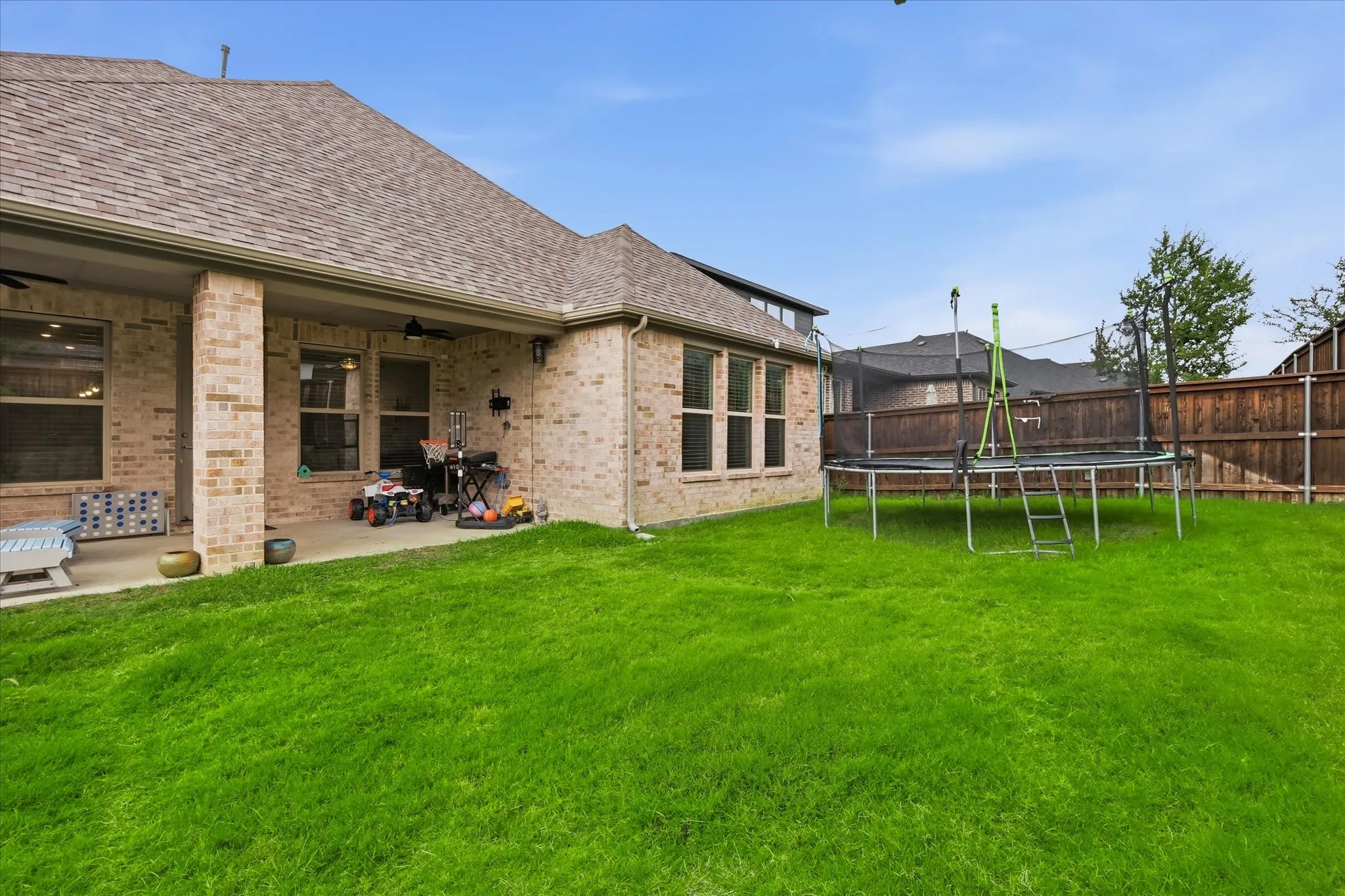 Expansive green lawn, brick exterior, covered patio, multiple windows, and a privacy fence