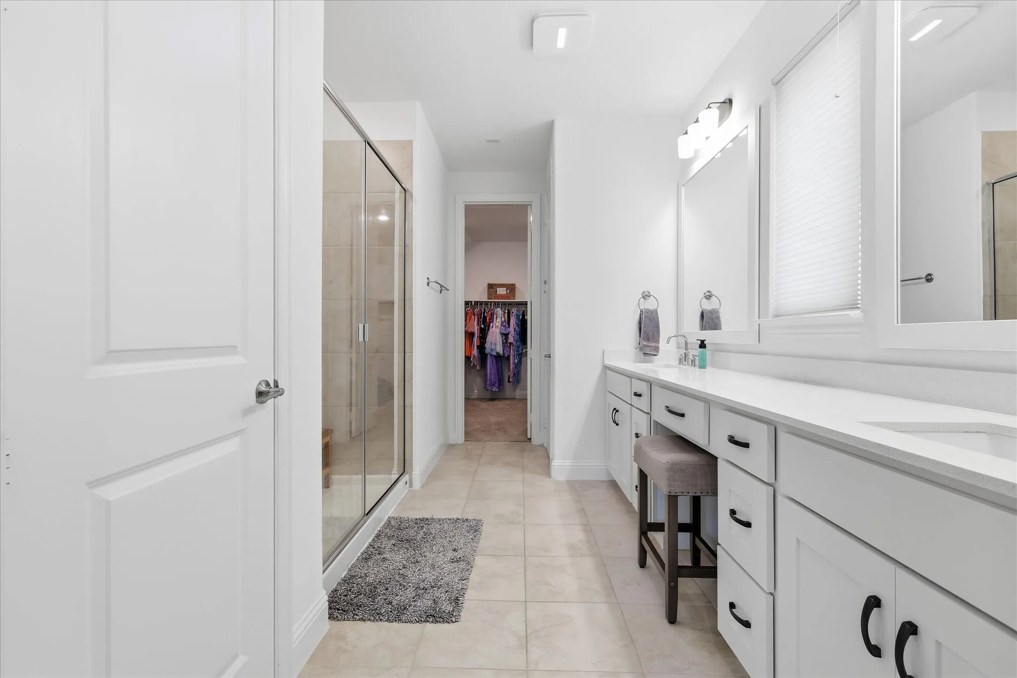 White shaker-style cabinetry with black hardware, stone countertop, dual undermount sinks, and a glass-enclosed shower