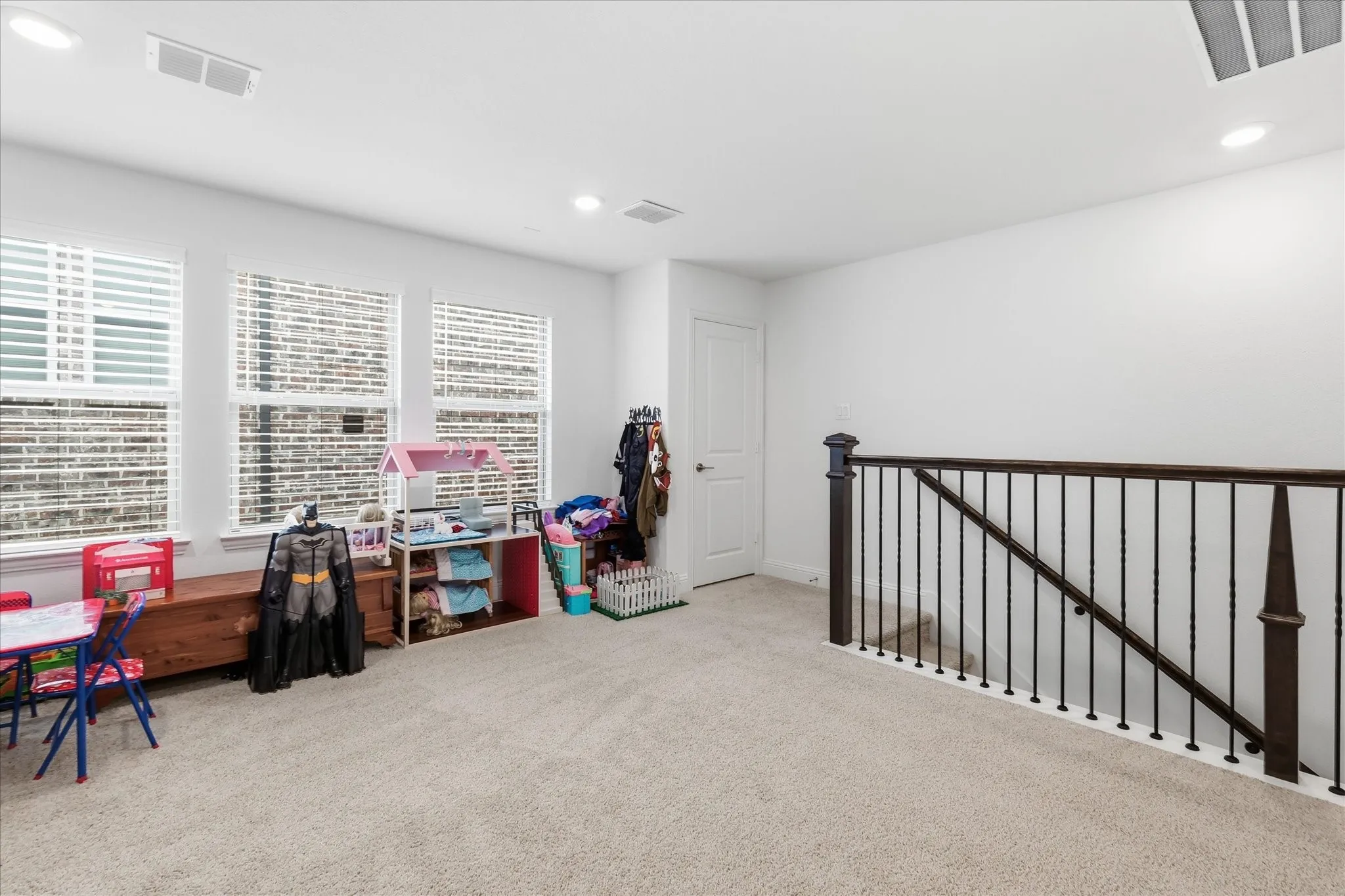 Carpeted room featuring three windows with blinds, a white door, and a staircase with dark wood railings and black iron balusters