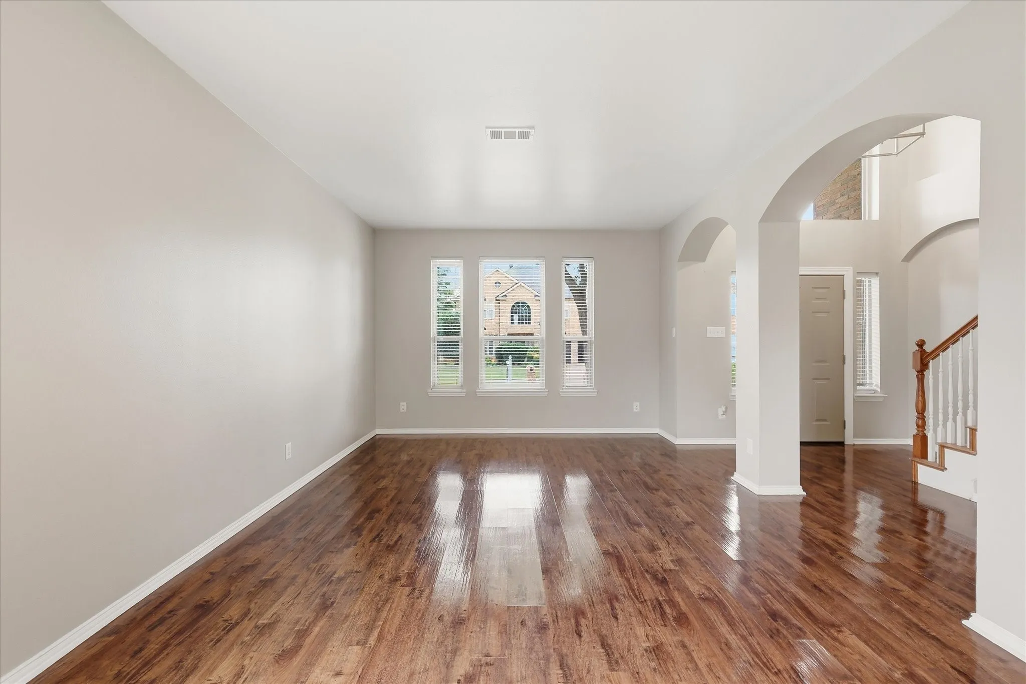 Expansive interior with wood-finish flooring, multiple arched doorways, and a staircase with a wooden handrail