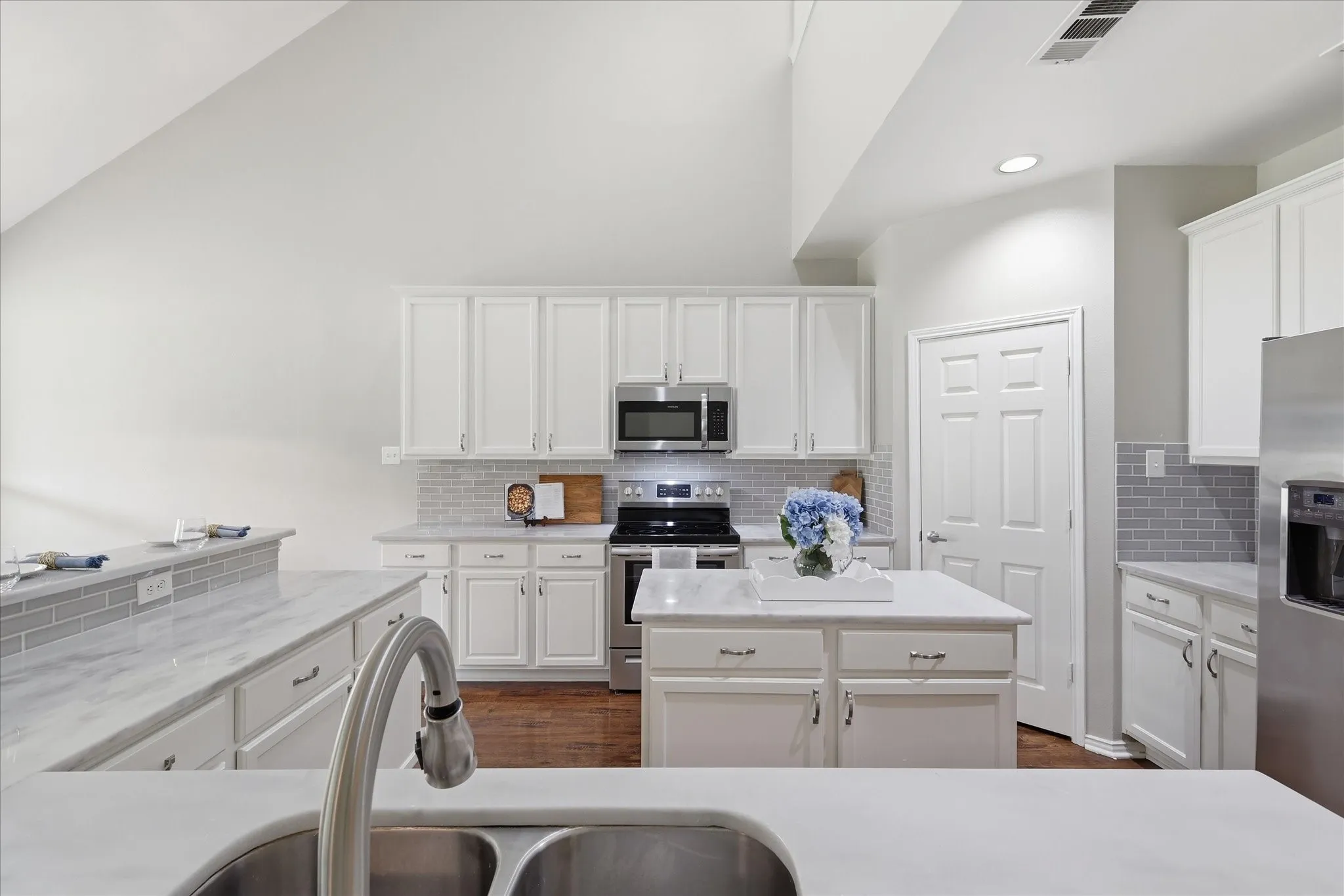Kitchen featuring white cabinetry, light-colored countertops, stainless steel appliances, a center island, and a tile backsplash