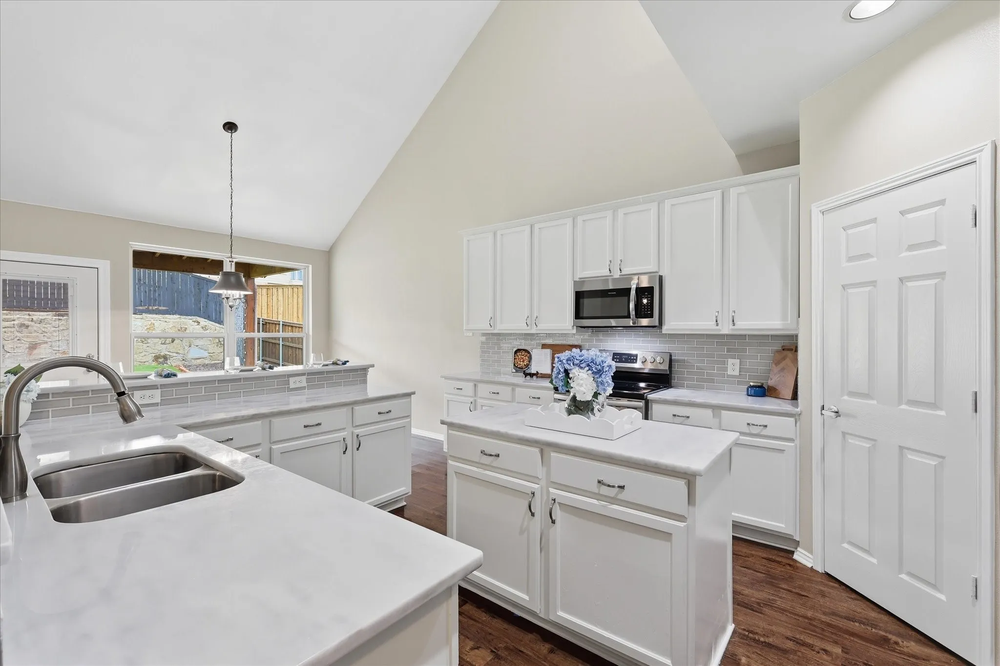 Vaulted ceiling with recessed lighting, white cabinetry, stainless steel appliances, stone-finish countertops, and wood-finish flooring