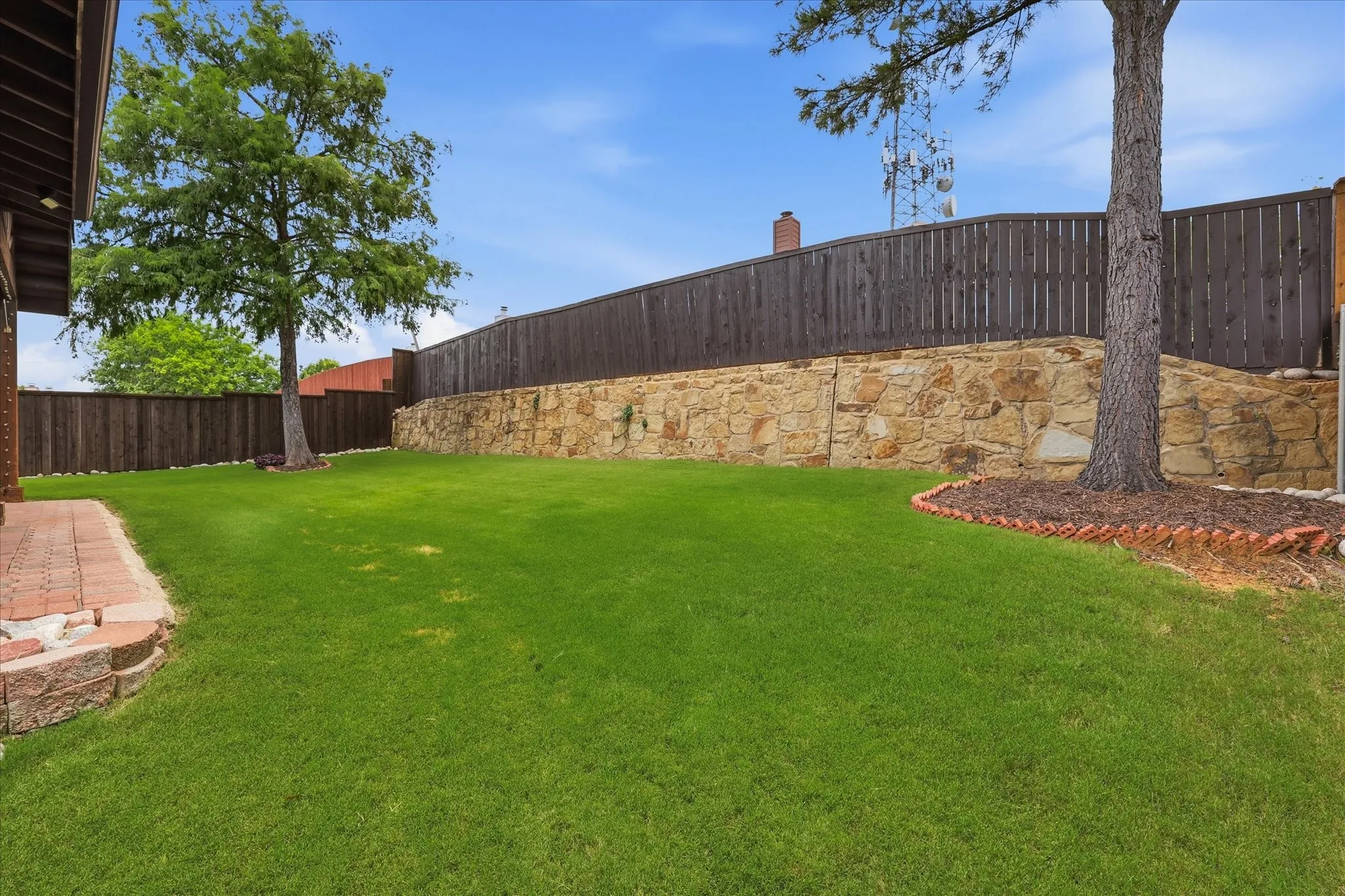Expansive lawn area with a stone retaining wall, mature trees, and a privacy fence