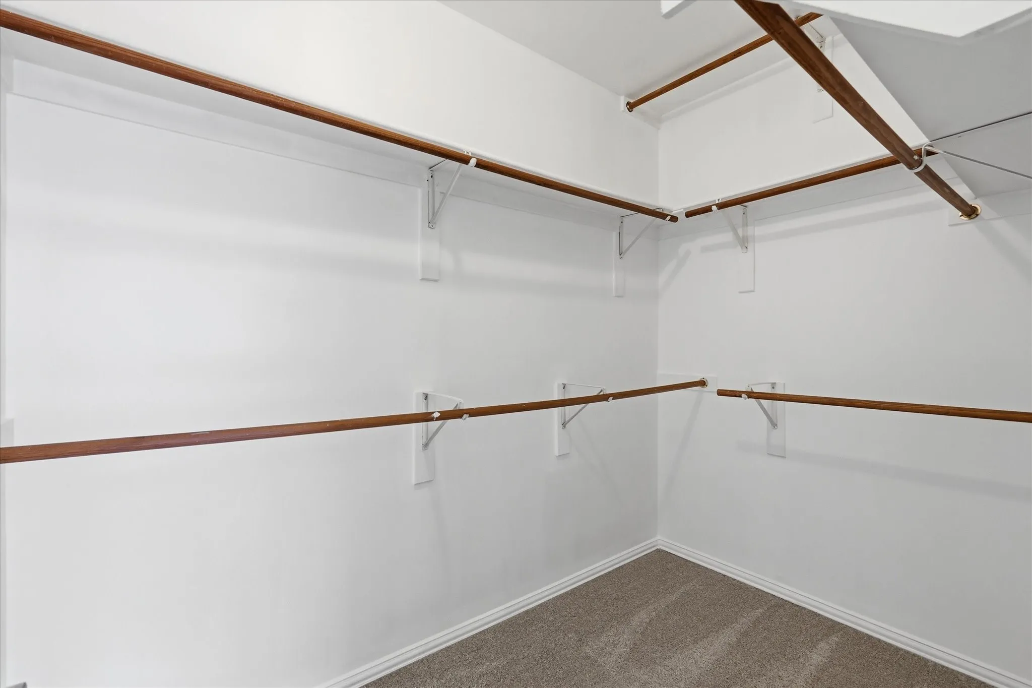 Customizable closet system with multiple wood-finish rods, white shelving supports, and neutral carpeting