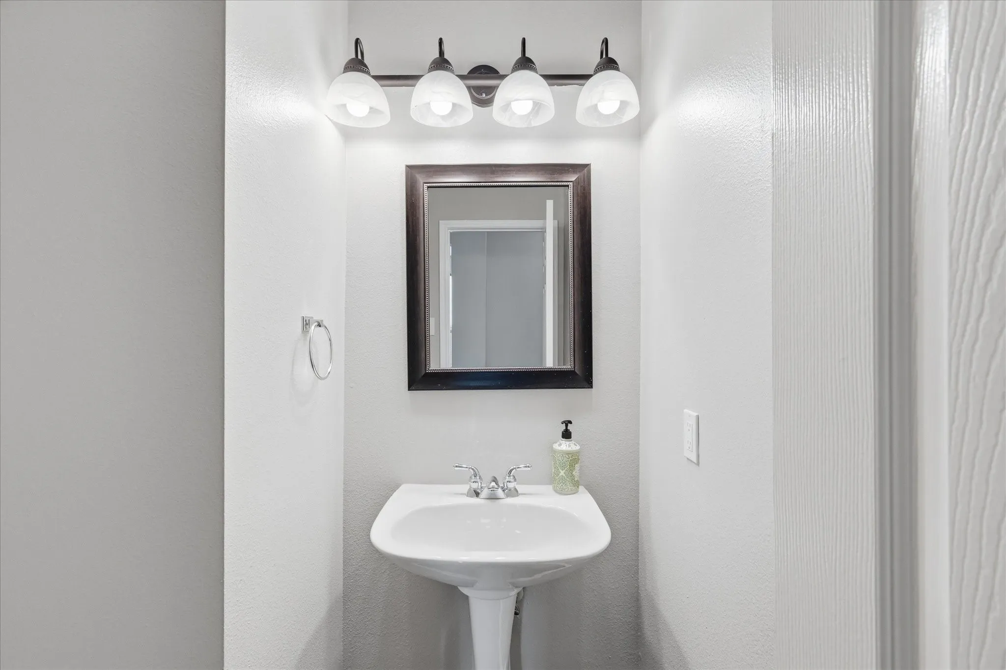 Pedestal sink with chrome faucet, framed mirror, and a four-light vanity fixture