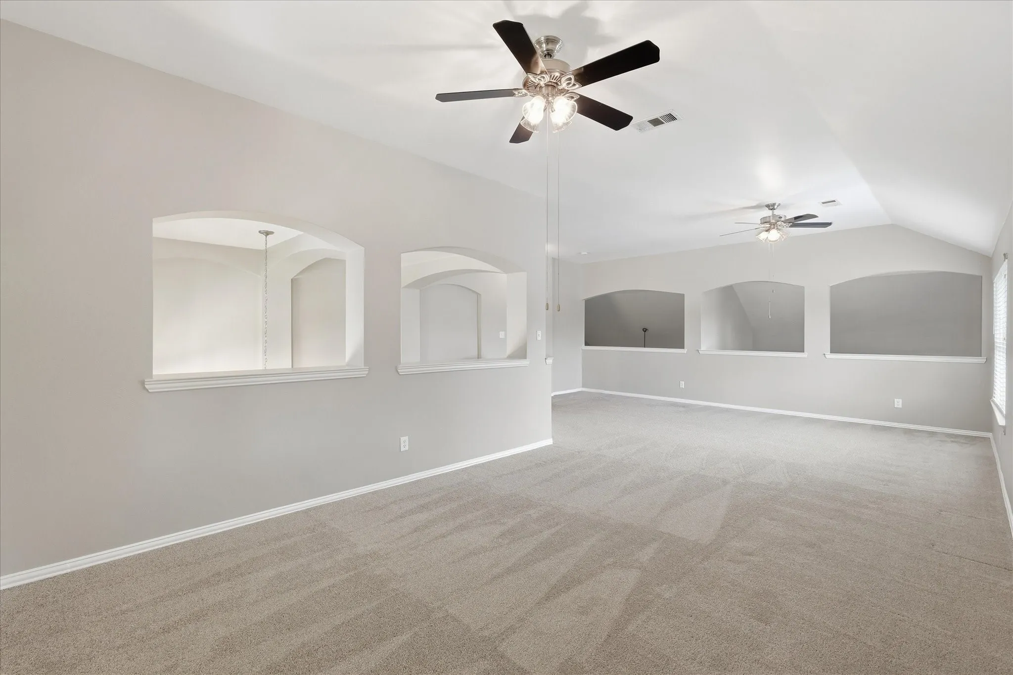 Expansive room with vaulted ceilings, recessed wall niches, and neutral carpeting