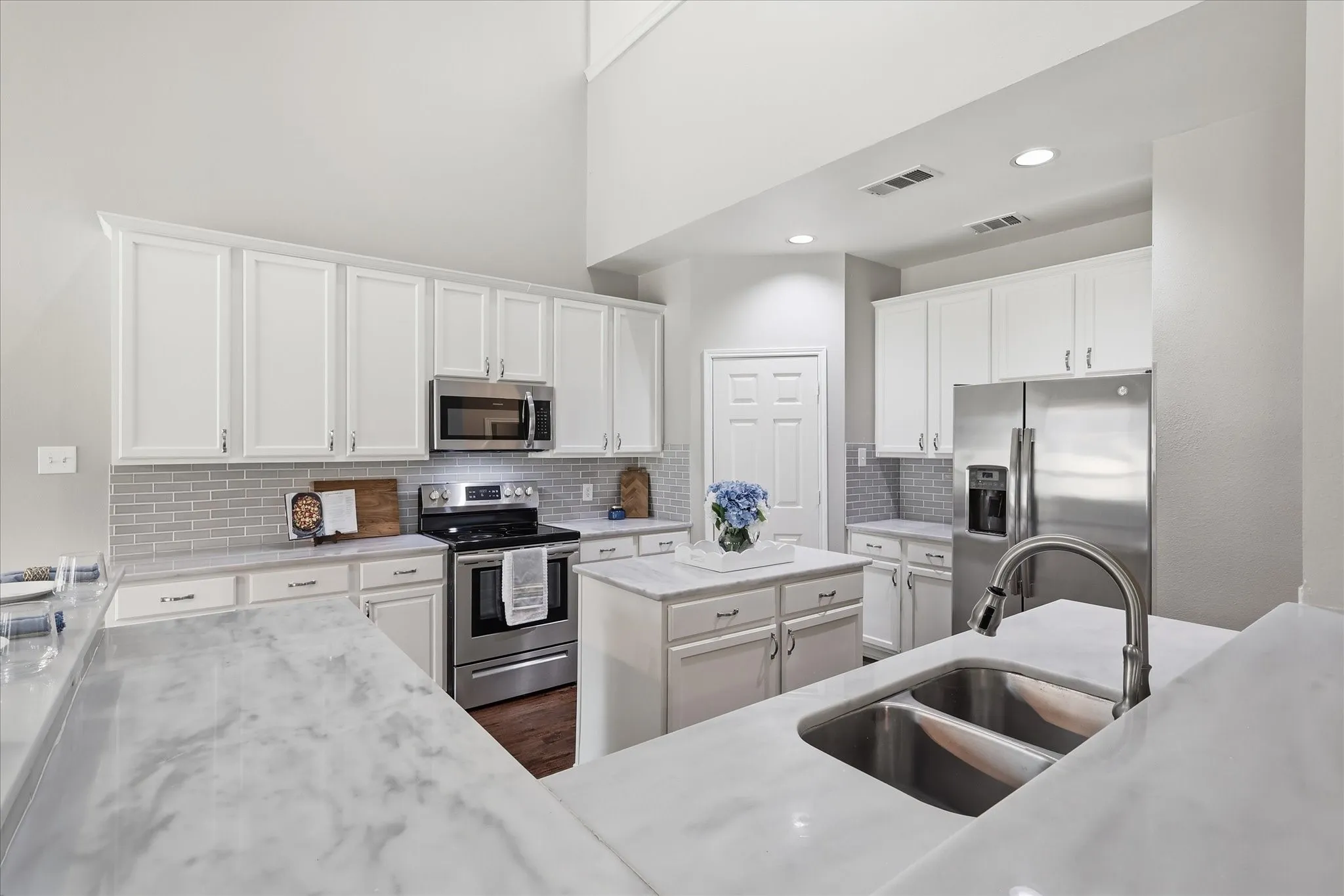 Kitchen featuring a large island, stainless steel appliances, white cabinetry, undermount double-basin sink, and a tile backsplash