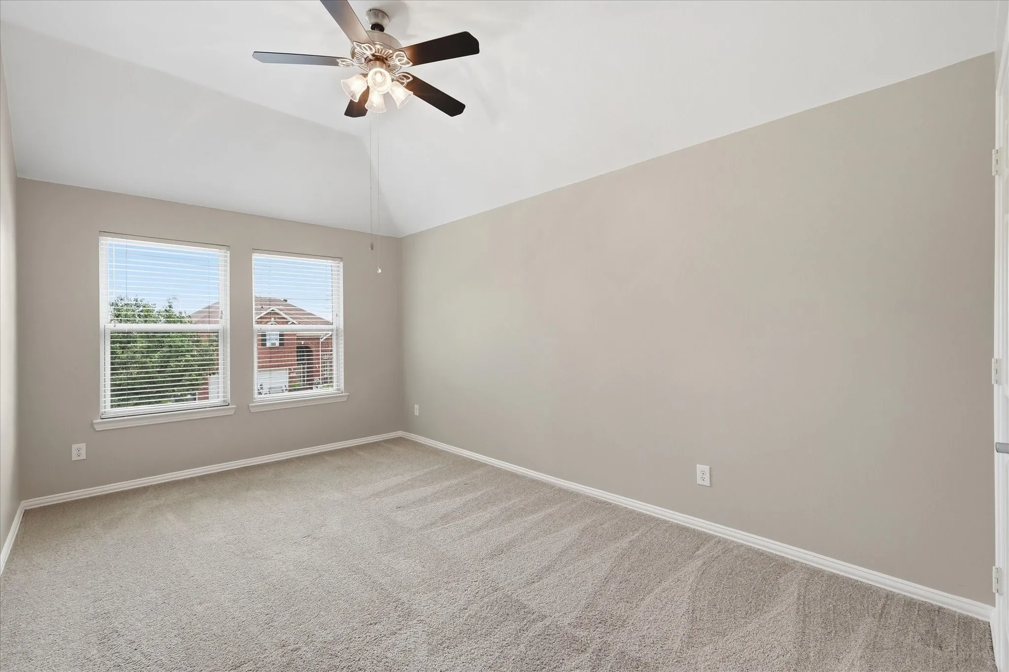 Vaulted ceiling with a ceiling fan, two windows with blinds, neutral-toned walls, and carpeted flooring