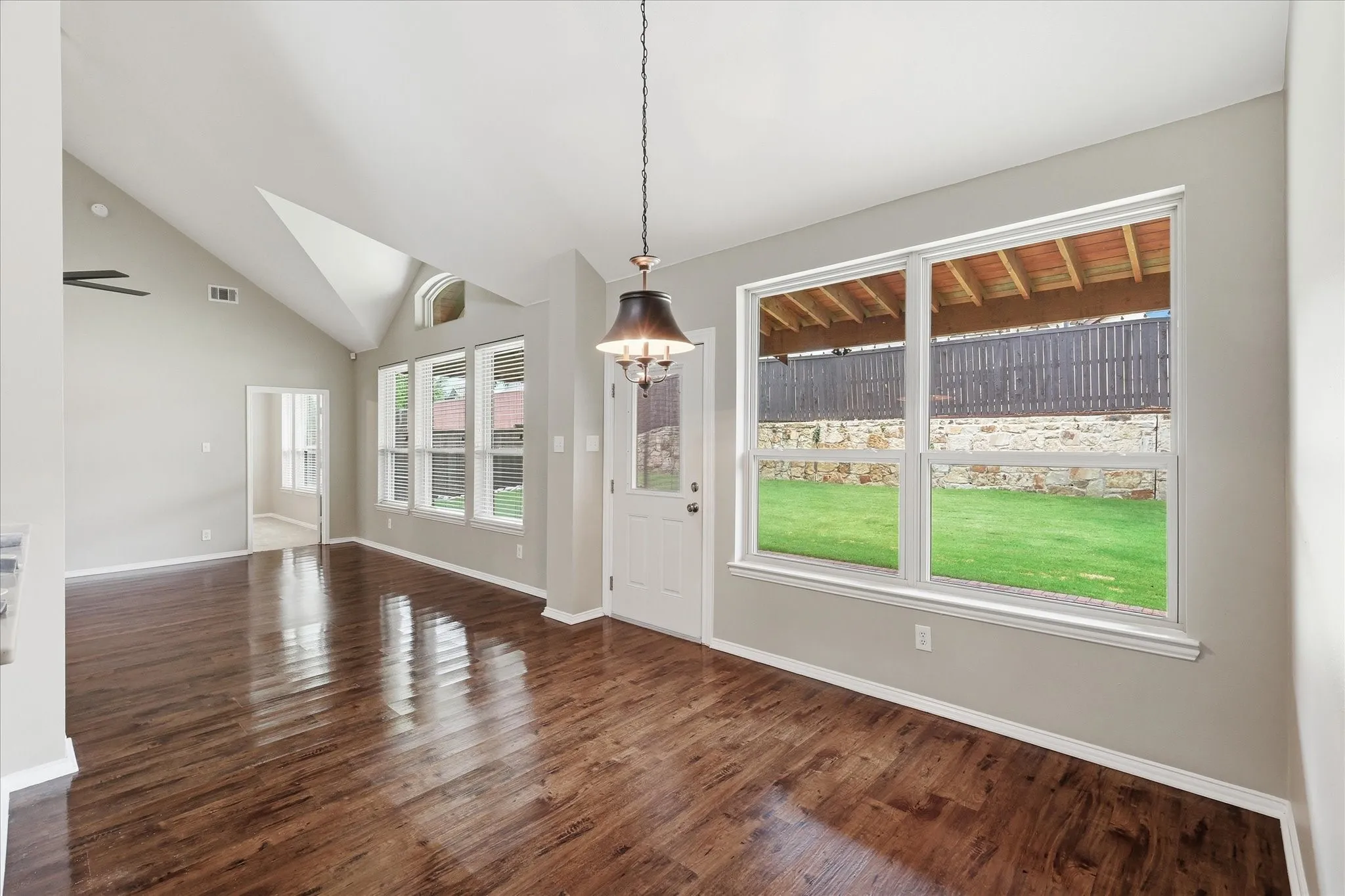Vaulted ceiling, wood-finish flooring, multiple windows, built-in chandelier, and a white door with an integrated window