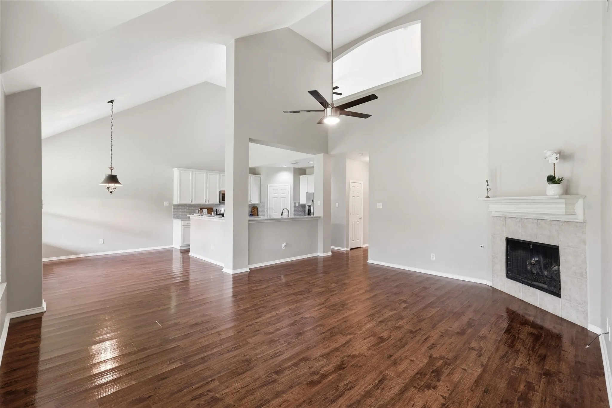 Vaulted ceiling, wood-finish flooring, ceiling fan, fireplace with tile surround, and built-in white cabinetry