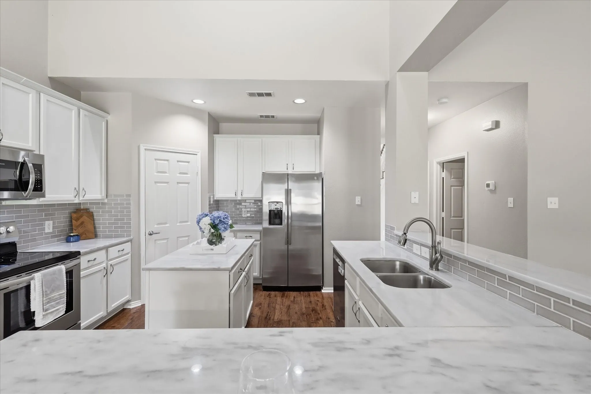 Kitchen featuring white cabinetry, stainless steel appliances, a center island, light-toned countertops, and a gray subway tile backsplash