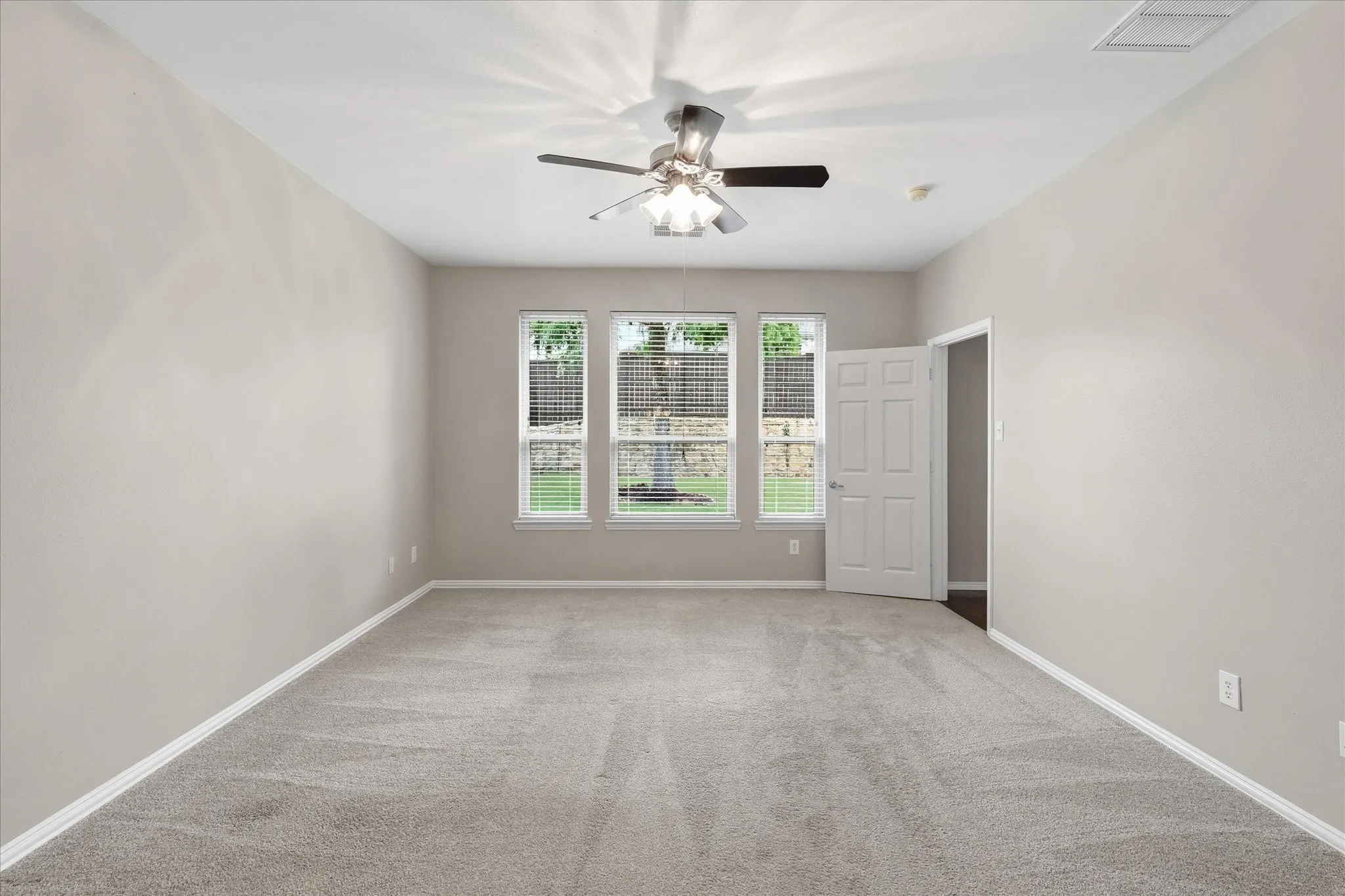 Spacious room featuring neutral carpeting, a ceiling fan with integrated lighting, and three large windows