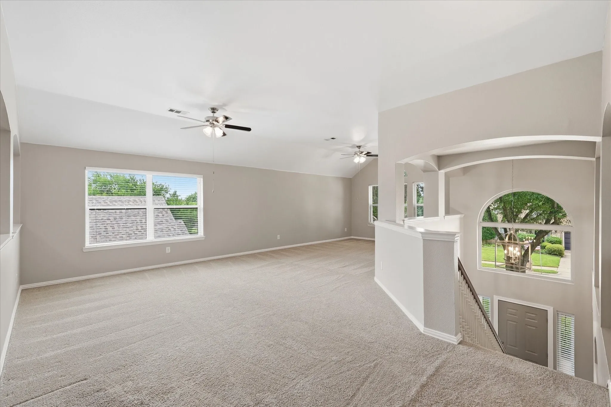Spacious carpeted area featuring vaulted ceilings, multiple windows, and ceiling fans