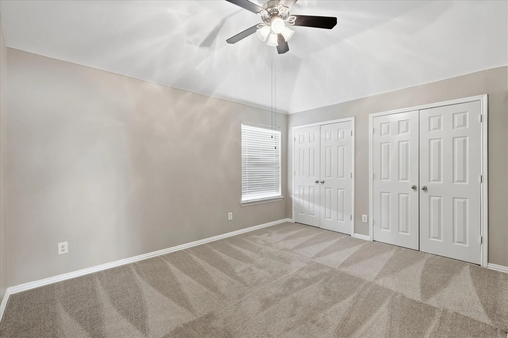 Vaulted ceiling with a ceiling fan, two closet systems with bifold doors, window with horizontal blinds, and neutral carpet flooring