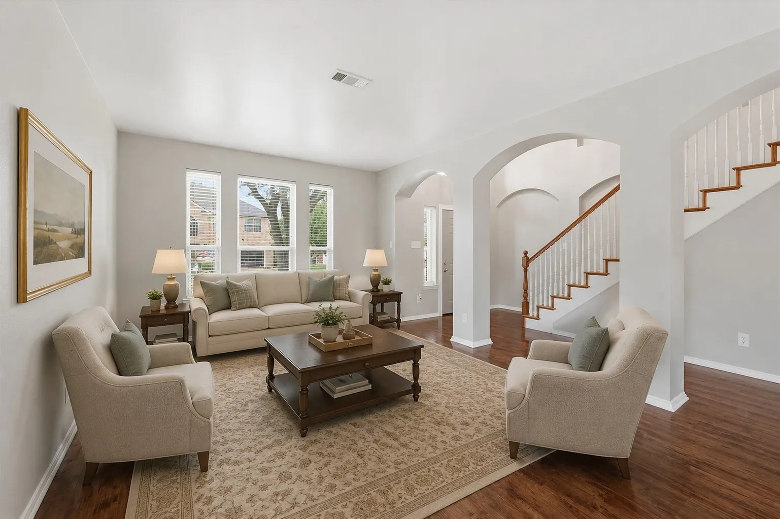 Spacious living area featuring wood-finish flooring, arched doorways, and a staircase with wood newel posts and handrails