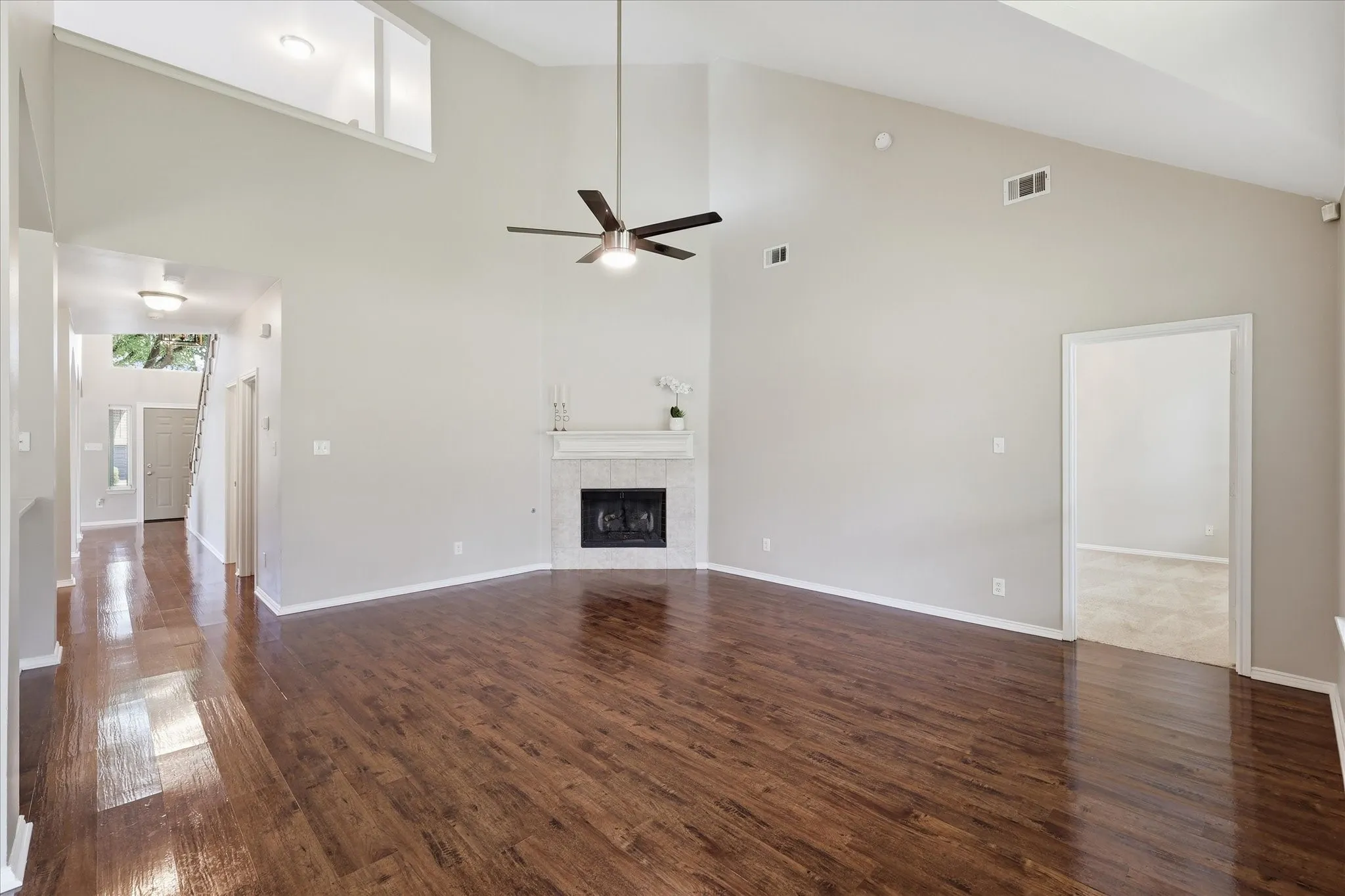 Spacious living area with high vaulted ceilings, wood-finish flooring, and a corner fireplace featuring a decorative mantle