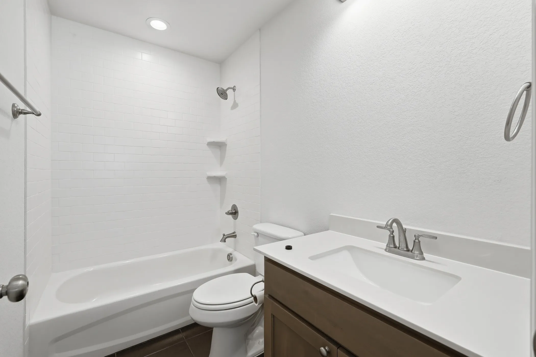 White subway tile shower surround with integrated shelves, a white bathtub, a toilet, a vanity with an integrated sink, and a brushed nickel faucet