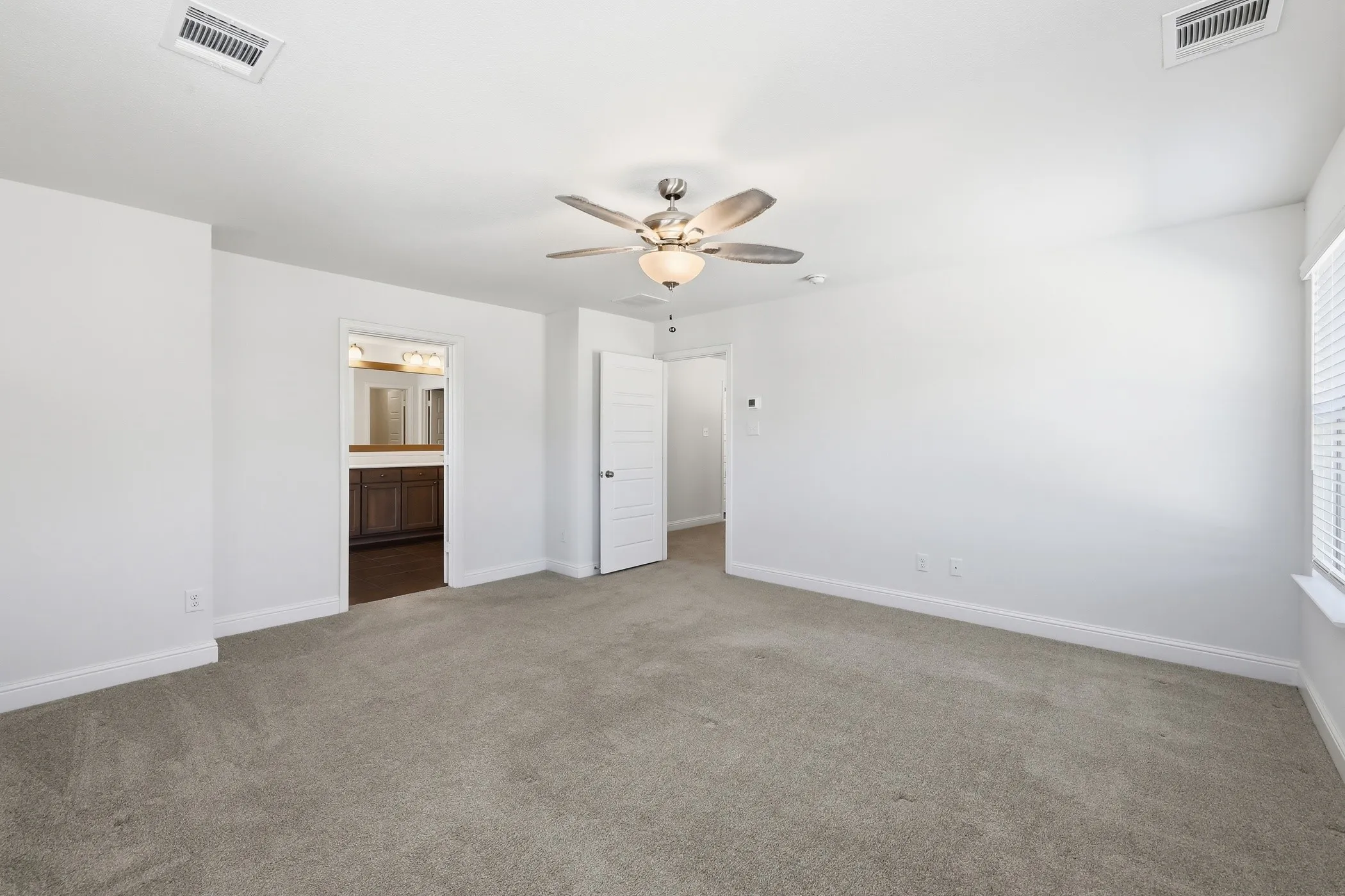 Plush gray carpeting throughout, featuring a ceiling fan with integrated lighting, white interior walls, and window blinds