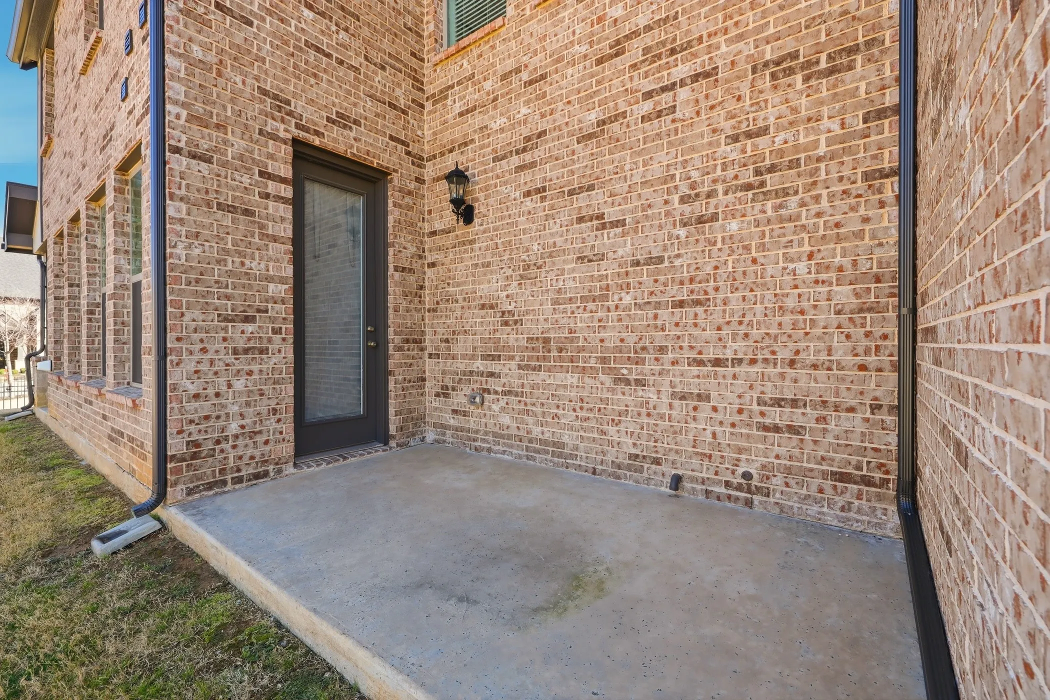 Brick exterior with a concrete patio, exterior door with full-light glass, and wall-mounted exterior light fixture