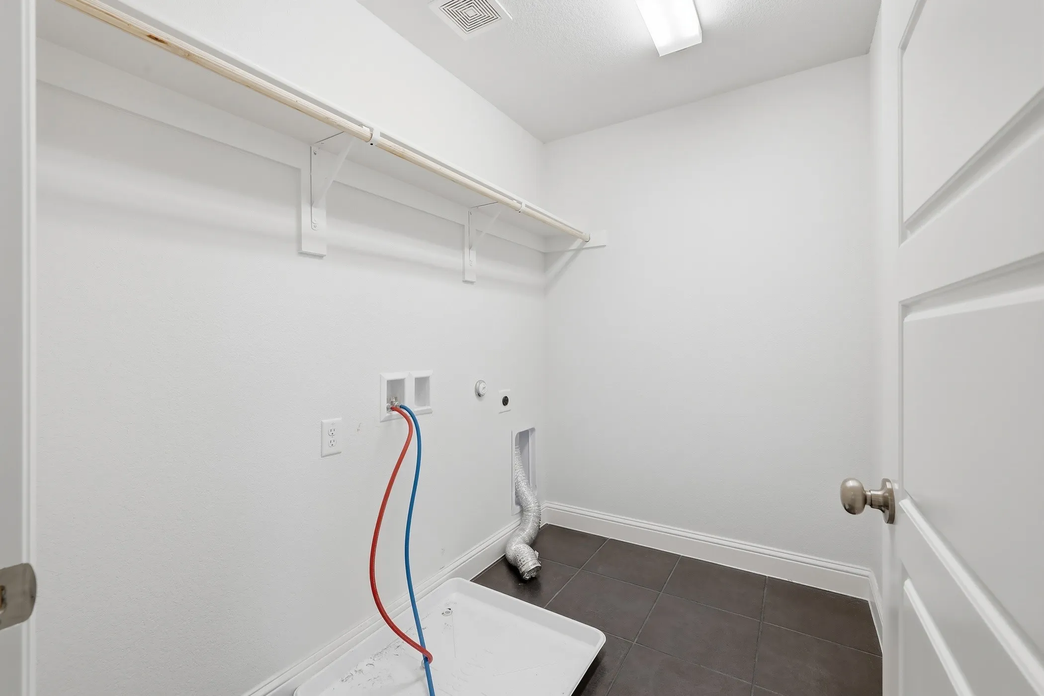 Laundry area featuring tile flooring, a utility sink connection, and a clothing rod with shelving