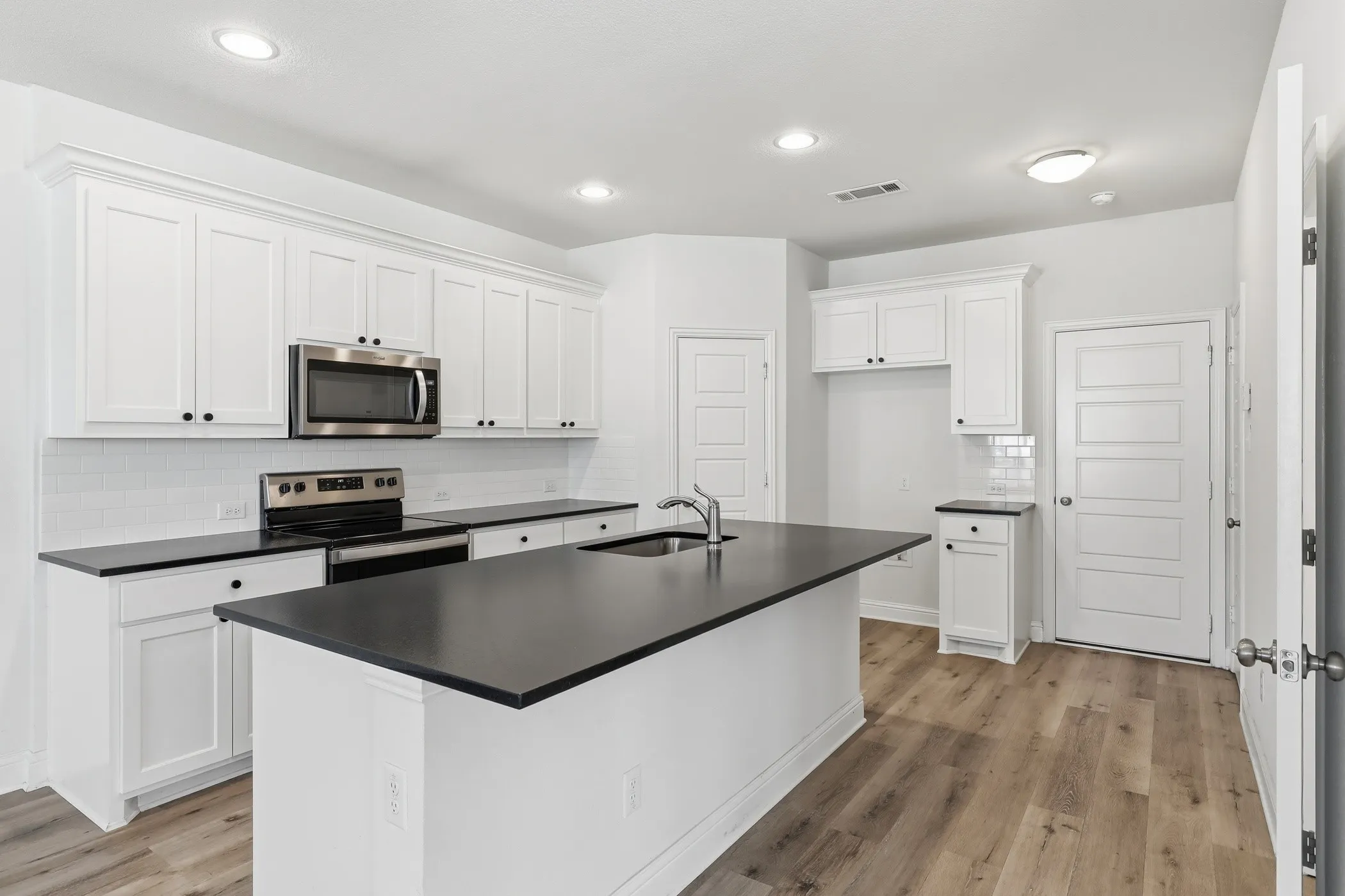 Kitchen featuring white cabinetry, dark countertops, stainless steel appliances, a white subway tile backsplash, and wood-finish flooring