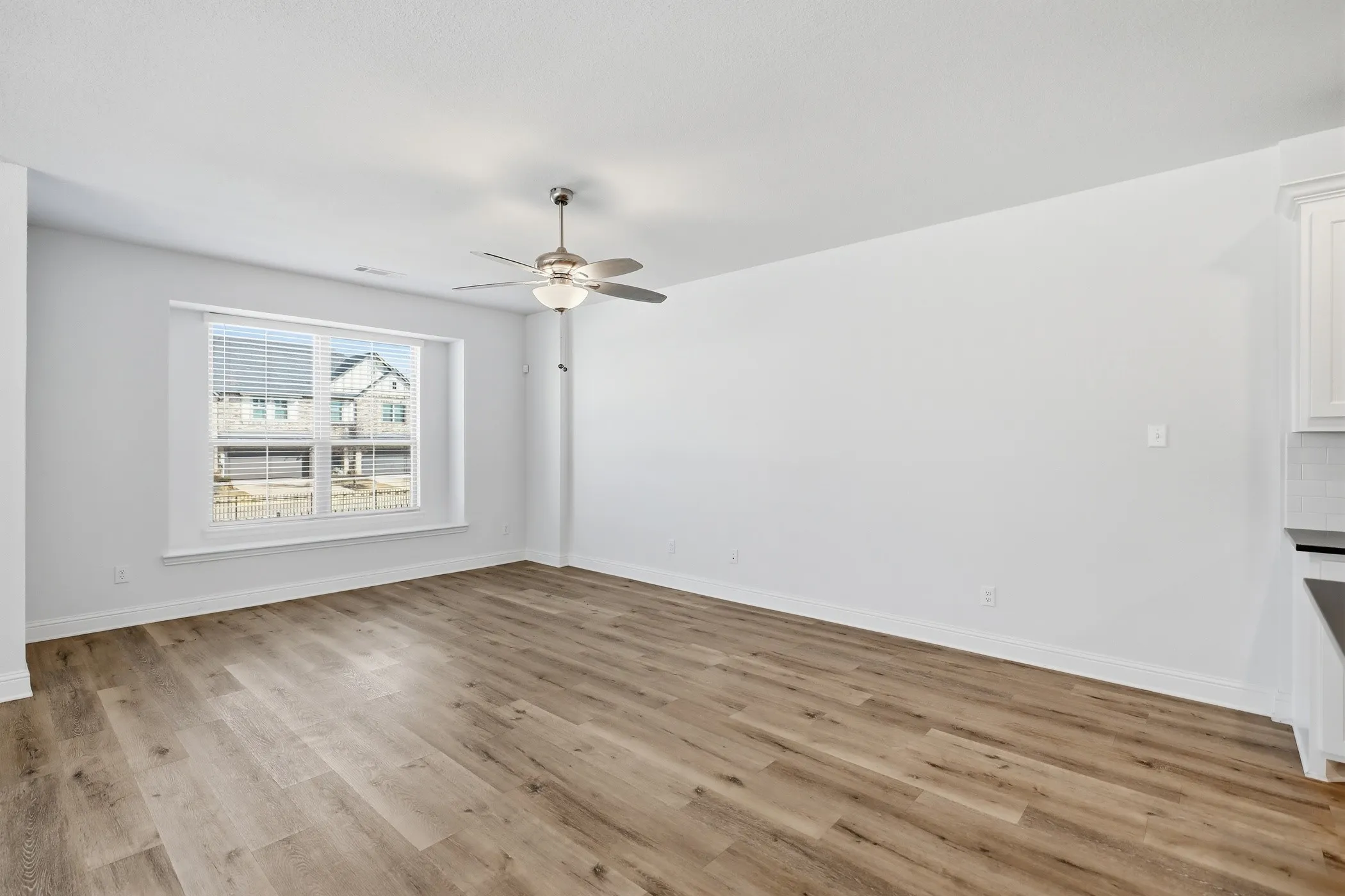 Spacious room featuring wood-finish flooring, a large window with blinds, and an overhead ceiling fan with integrated lighting