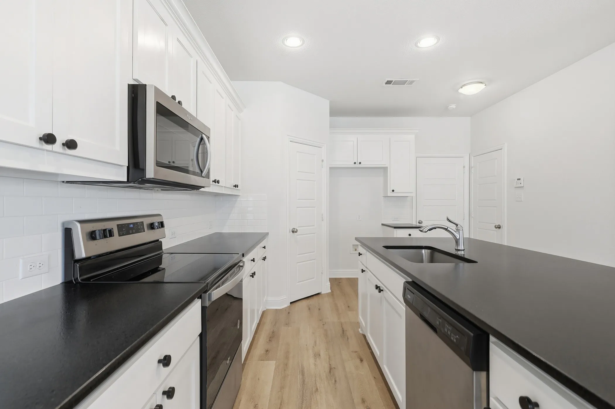 White cabinetry, black countertops, stainless steel appliances, white subway tile backsplash, and wood-finish flooring