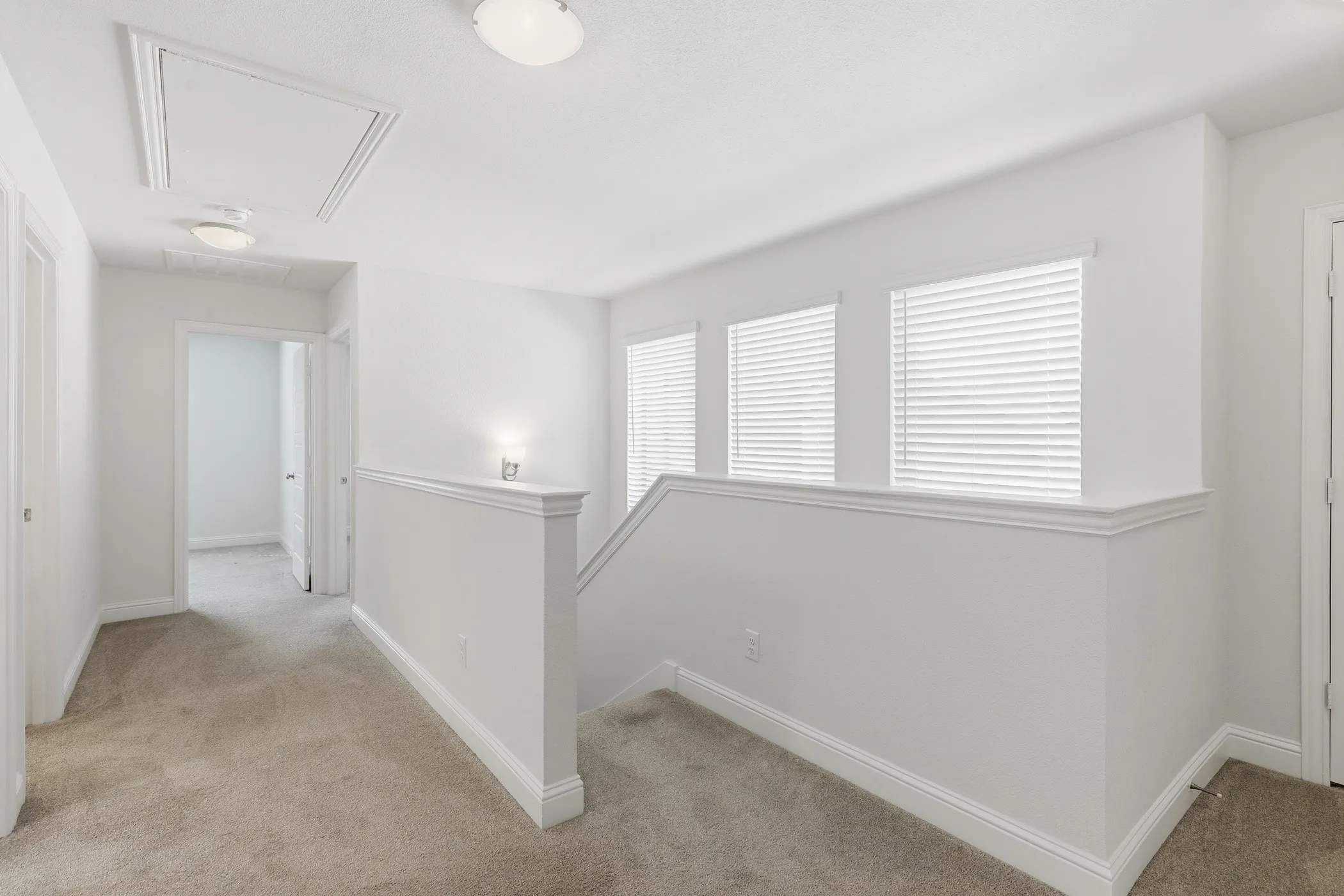 Carpeted hallway with three windows featuring blinds, a built-in wall sconce, and a ceiling-mounted light fixture
