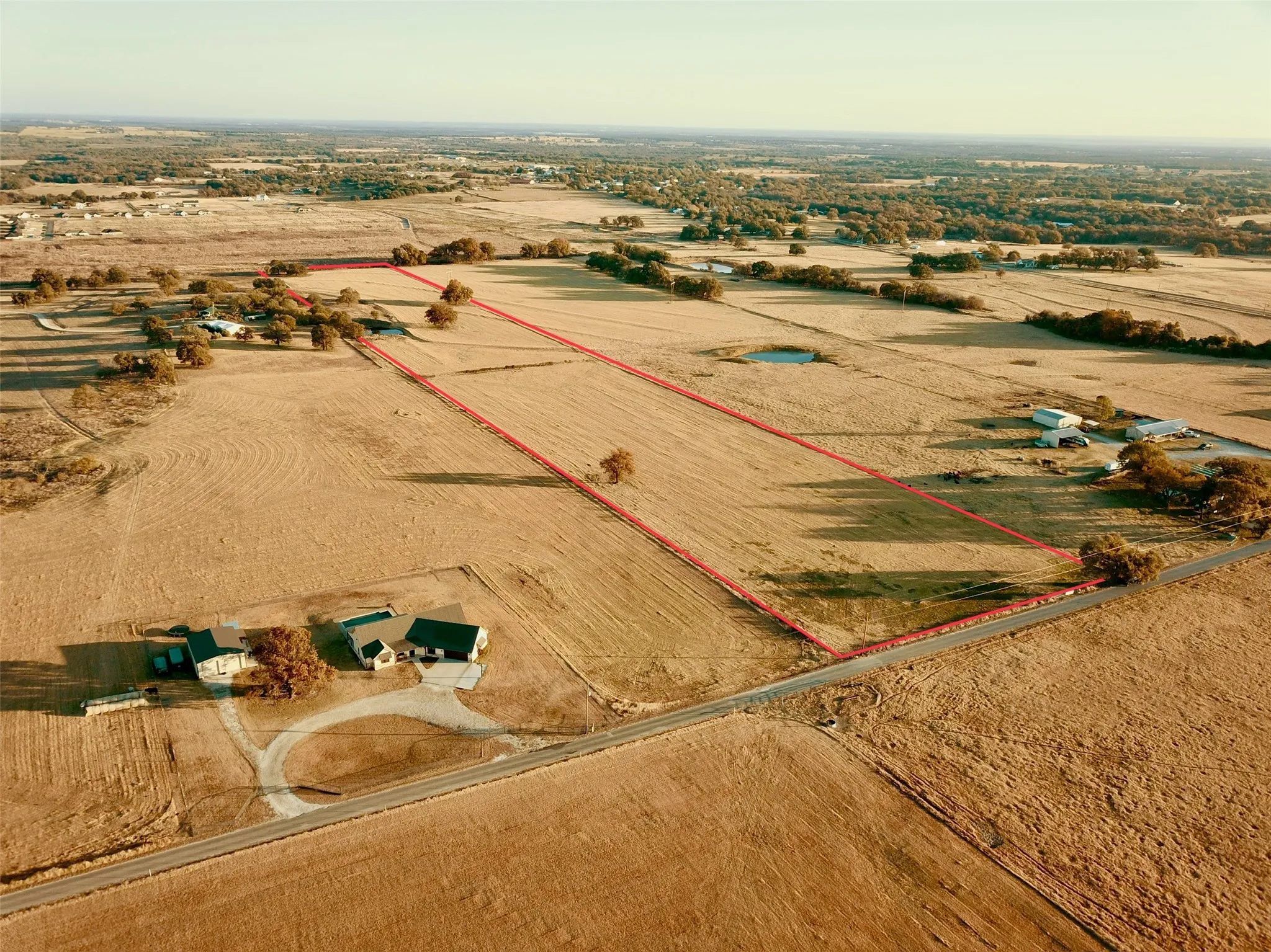 Expansive land parcel featuring a natural pond, scattered mature trees, and direct road frontage