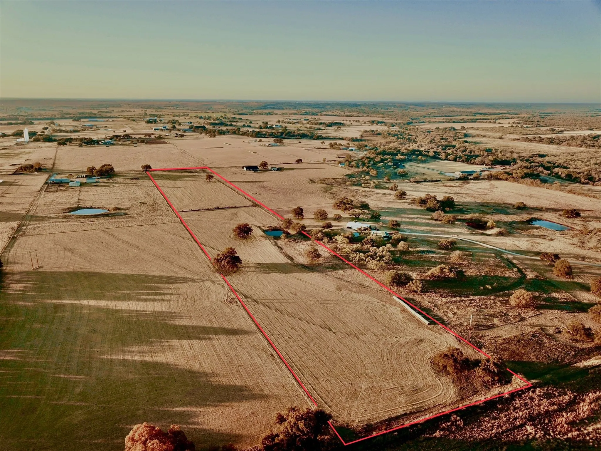 Expansive land parcel featuring open fields, scattered mature trees, and a distant water feature
