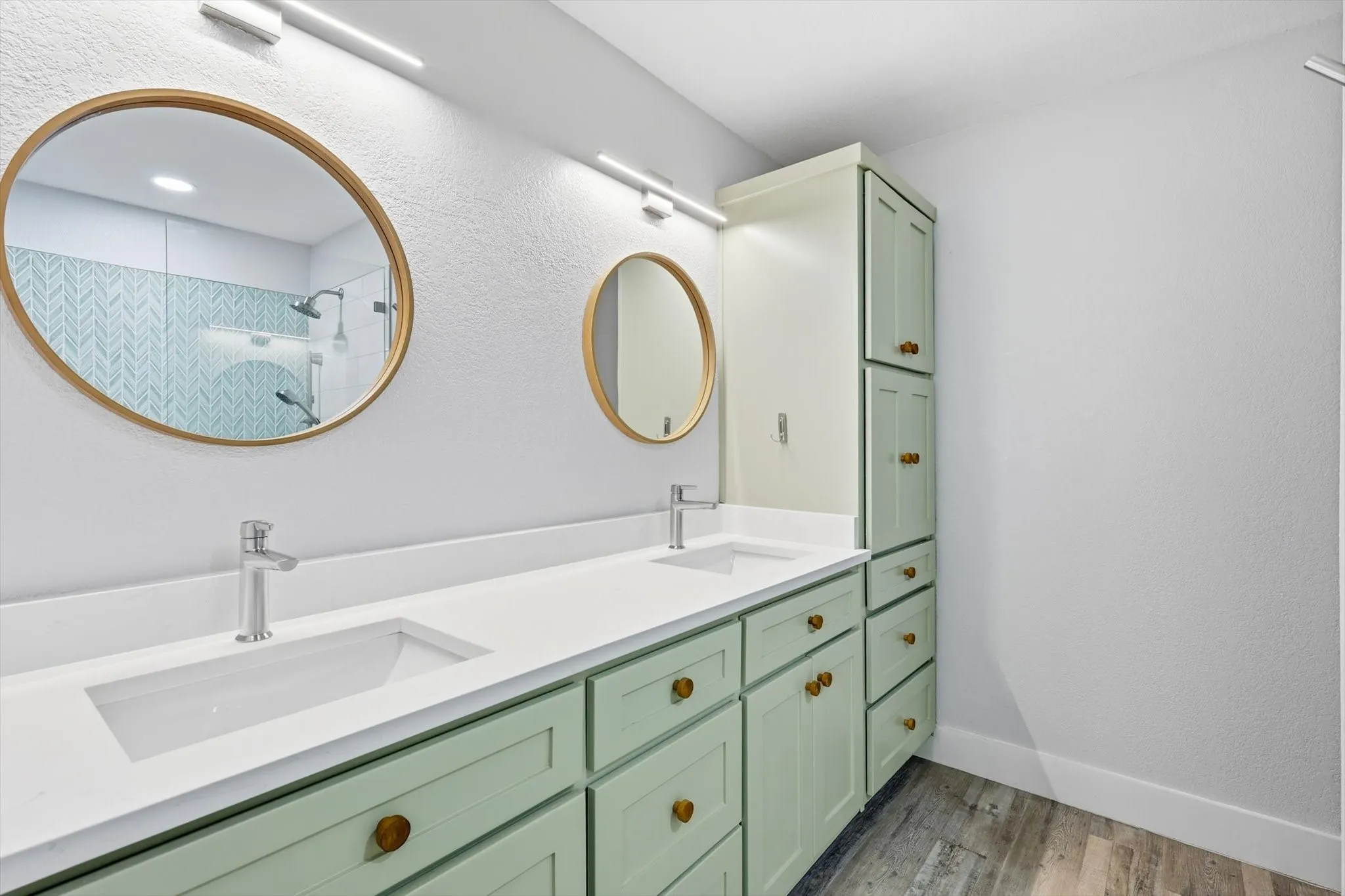 Spa-inspired primary bathroom featuring dual undermount sinks with a continuous white quartz countertop, soft-close cabinetry in sage green with brass hardware, and polished chrome faucetry