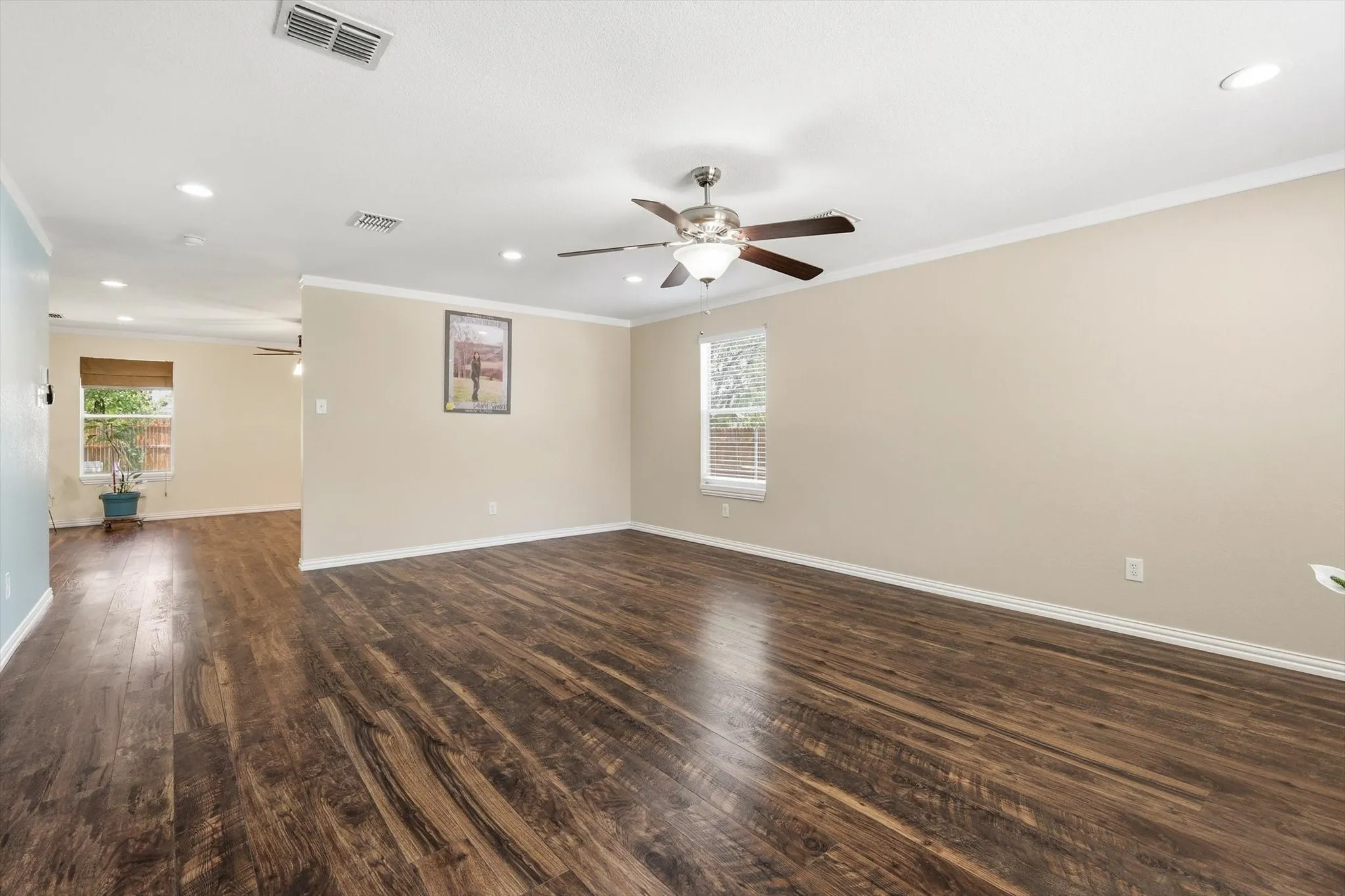 Spacious open-concept living area showcasing rich wood-finish flooring throughout, neutral wall finishes, recessed ceiling lighting, and a ceiling fan with brushed nickel accents