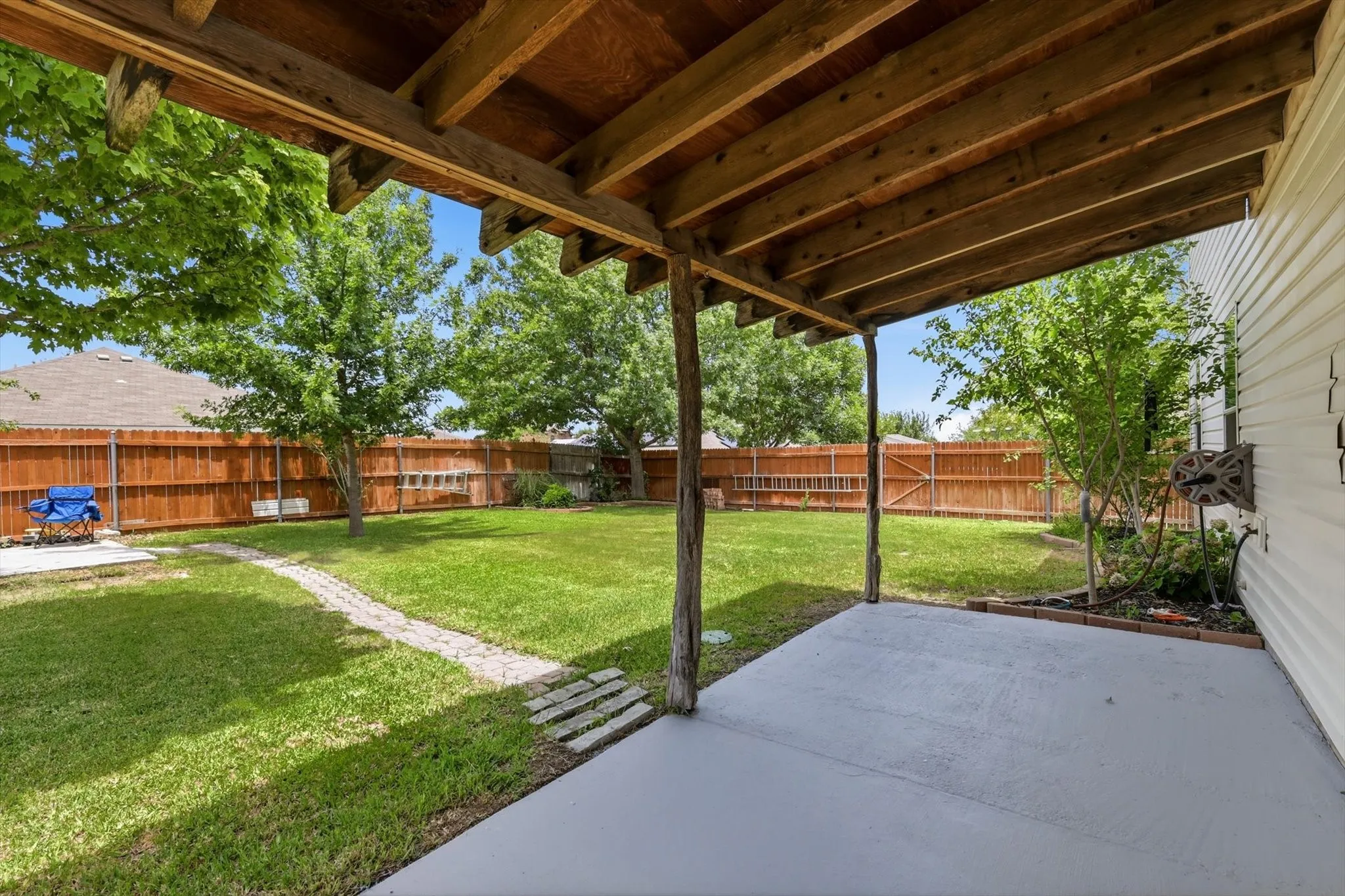 Expansive backyard oasis featuring a covered patio with exposed beam construction, concrete flooring, and mature shade trees