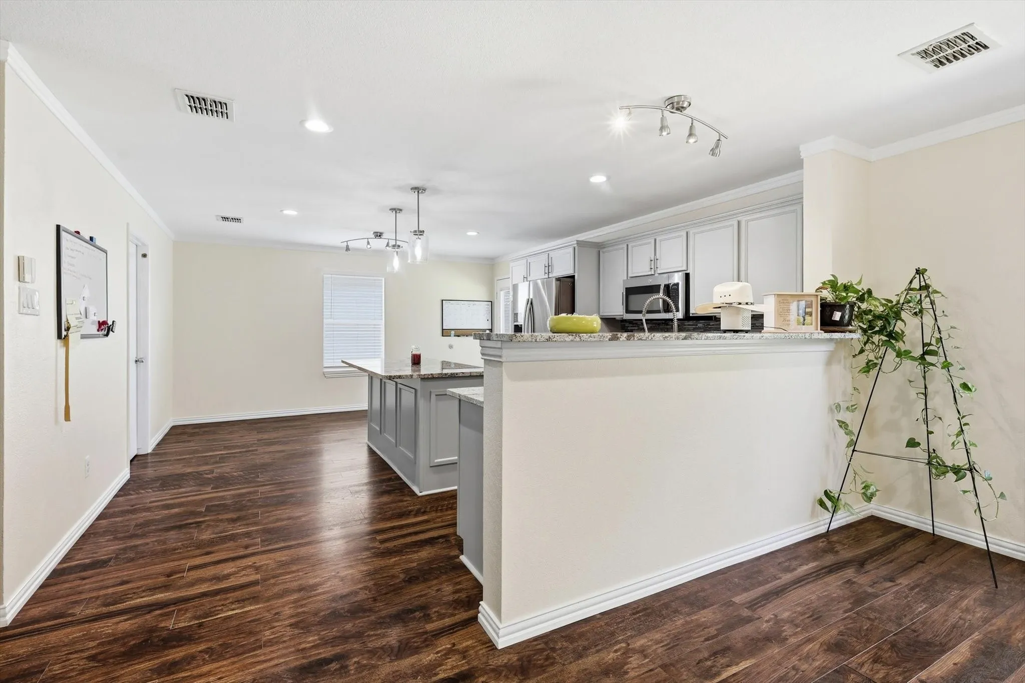 Modern kitchen featuring white cabinetry with a large center island, stainless steel appliances, recessed and pendant lighting, and wood-finish flooring throughout the open-concept space
