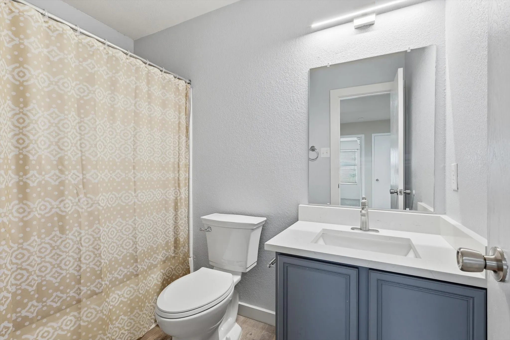 Modern bathroom featuring a dark blue vanity with white countertop and rectangular vessel sink, brushed nickel faucet, large framed mirror with integrated lighting, and a patterned shower curtain with coordinating tile surround