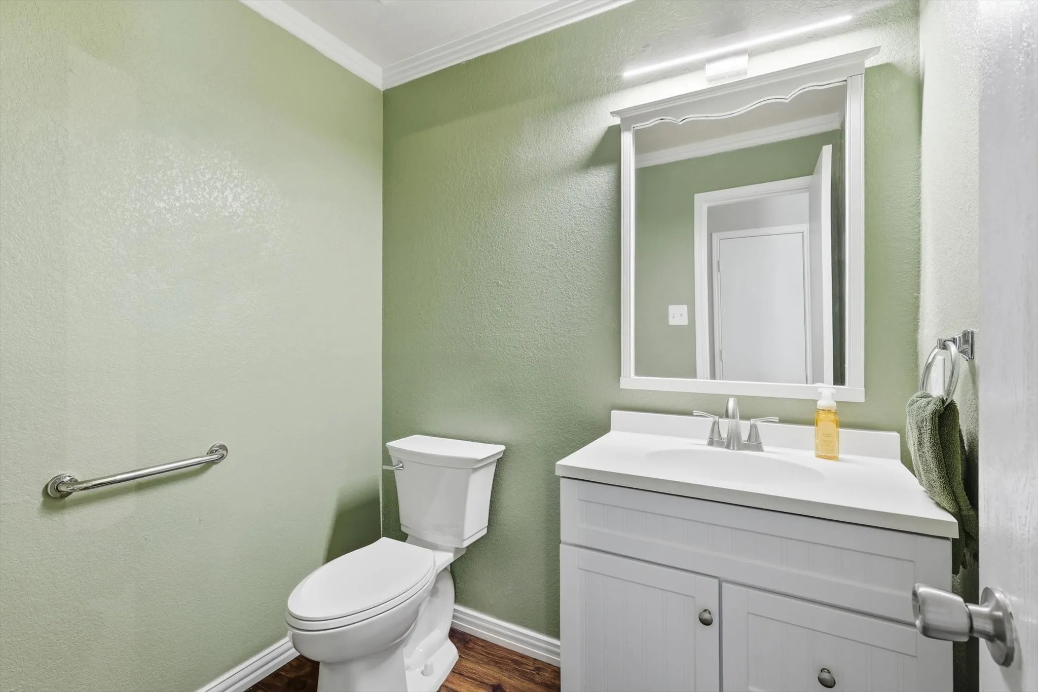 White vanity with a single basin sink, wall-mounted mirror, and wood-finish flooring
