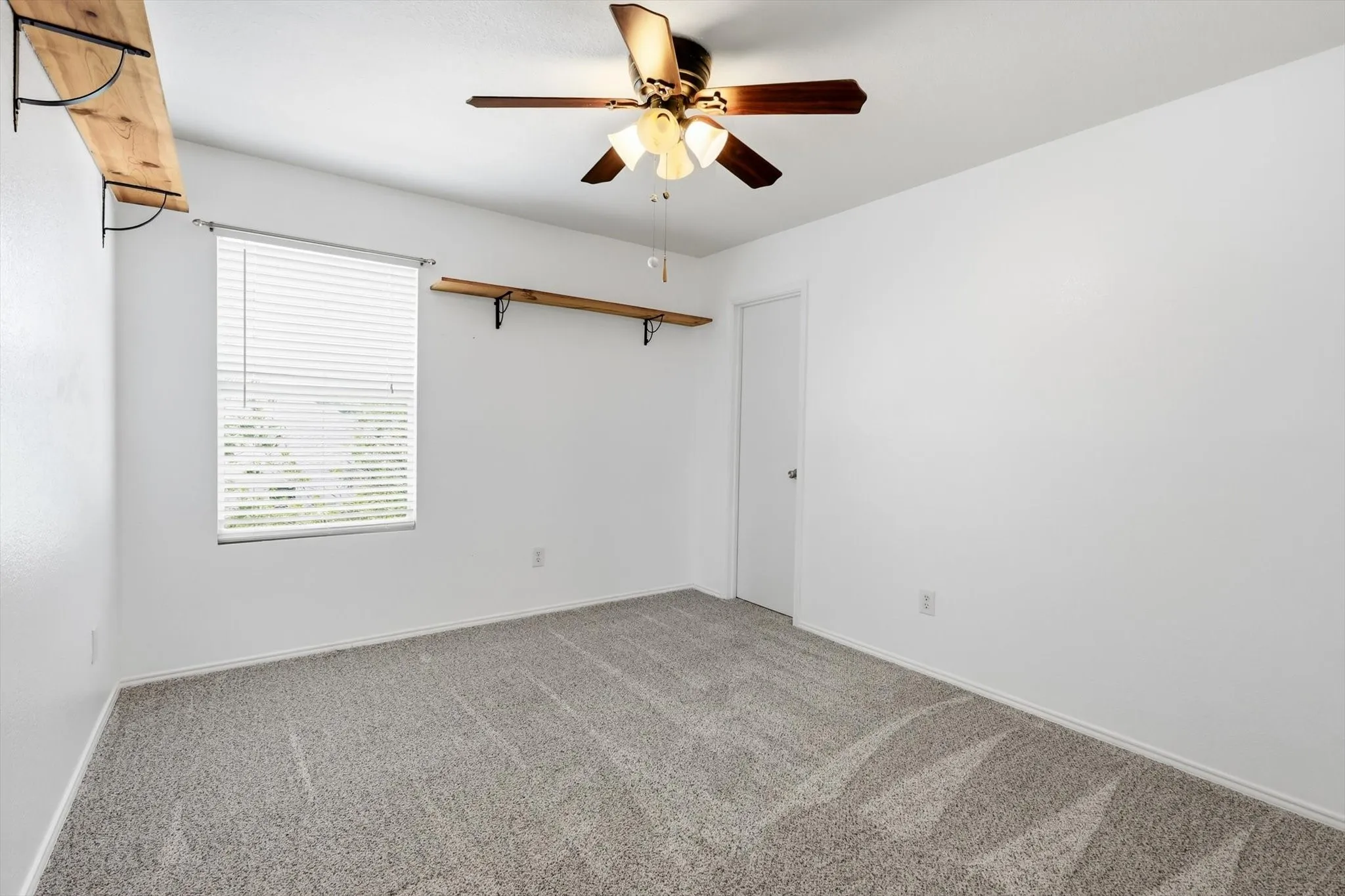 Bright bedroom offering neutral carpet flooring, a ceiling fan with integrated lighting, large window with blinds for natural light control, and white walls throughout