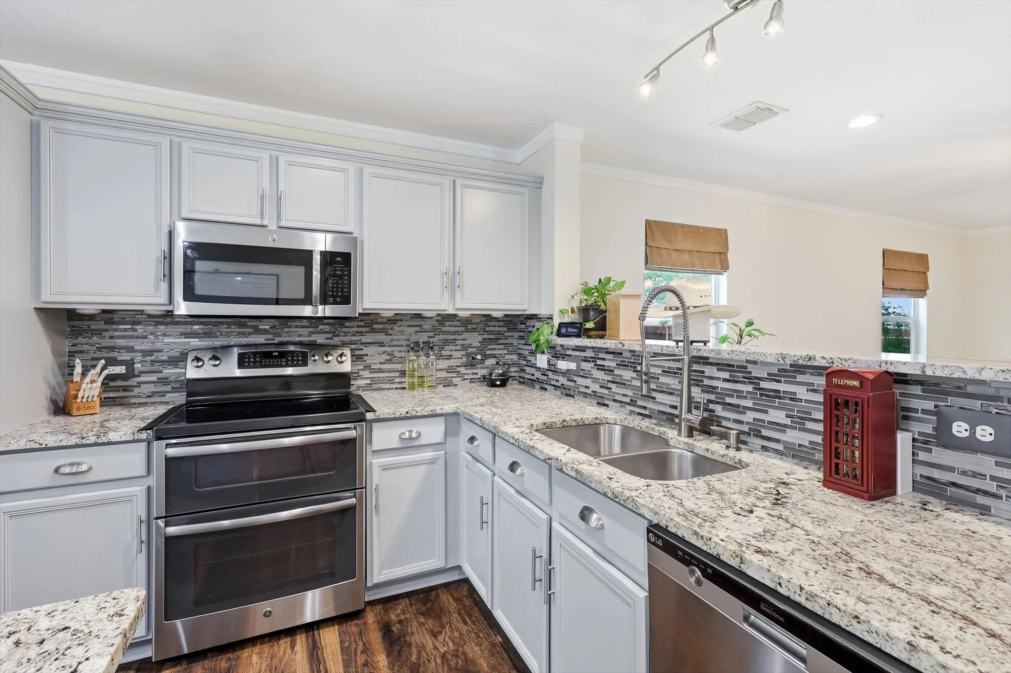 Kitchen featuring granite countertops, stainless steel appliances, a tile backsplash, light-toned cabinetry, and wood-finish flooring