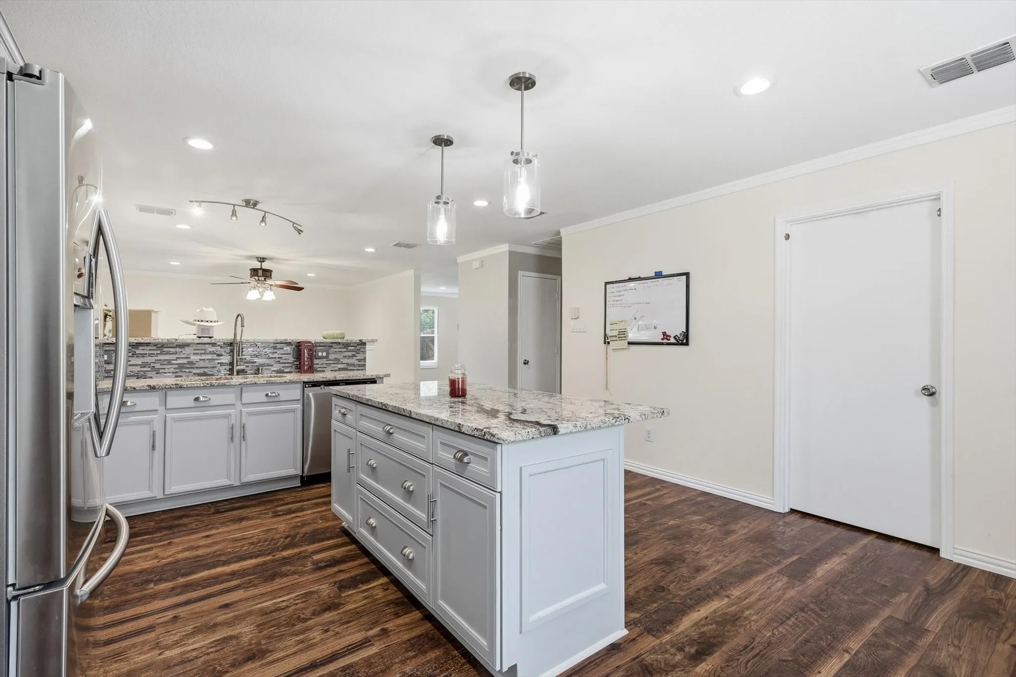 Renovated kitchen featuring white cabinetry, a large center island with granite countertops, stainless steel appliances, wood-finish flooring, and pendant lighting