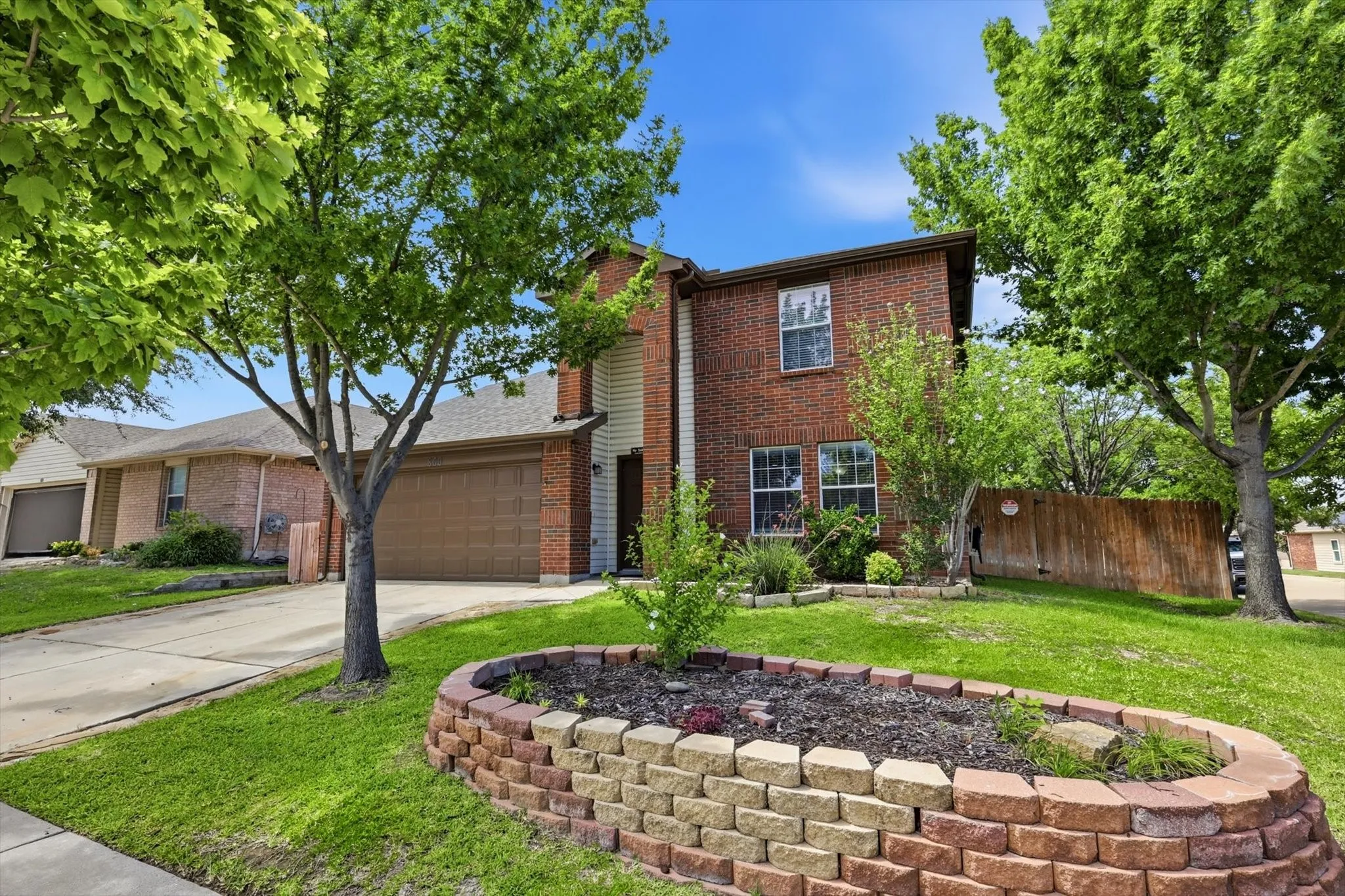 Brick Colonial home featuring a manicured front lawn with mature shade trees and a curved brick planter bed